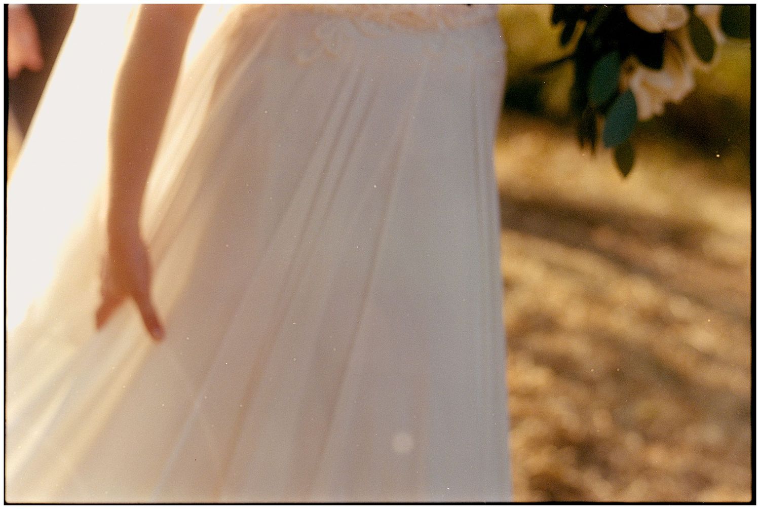 Close-up view of flowing white wedding dress fabric against a blurred natural outdoor backdrop.