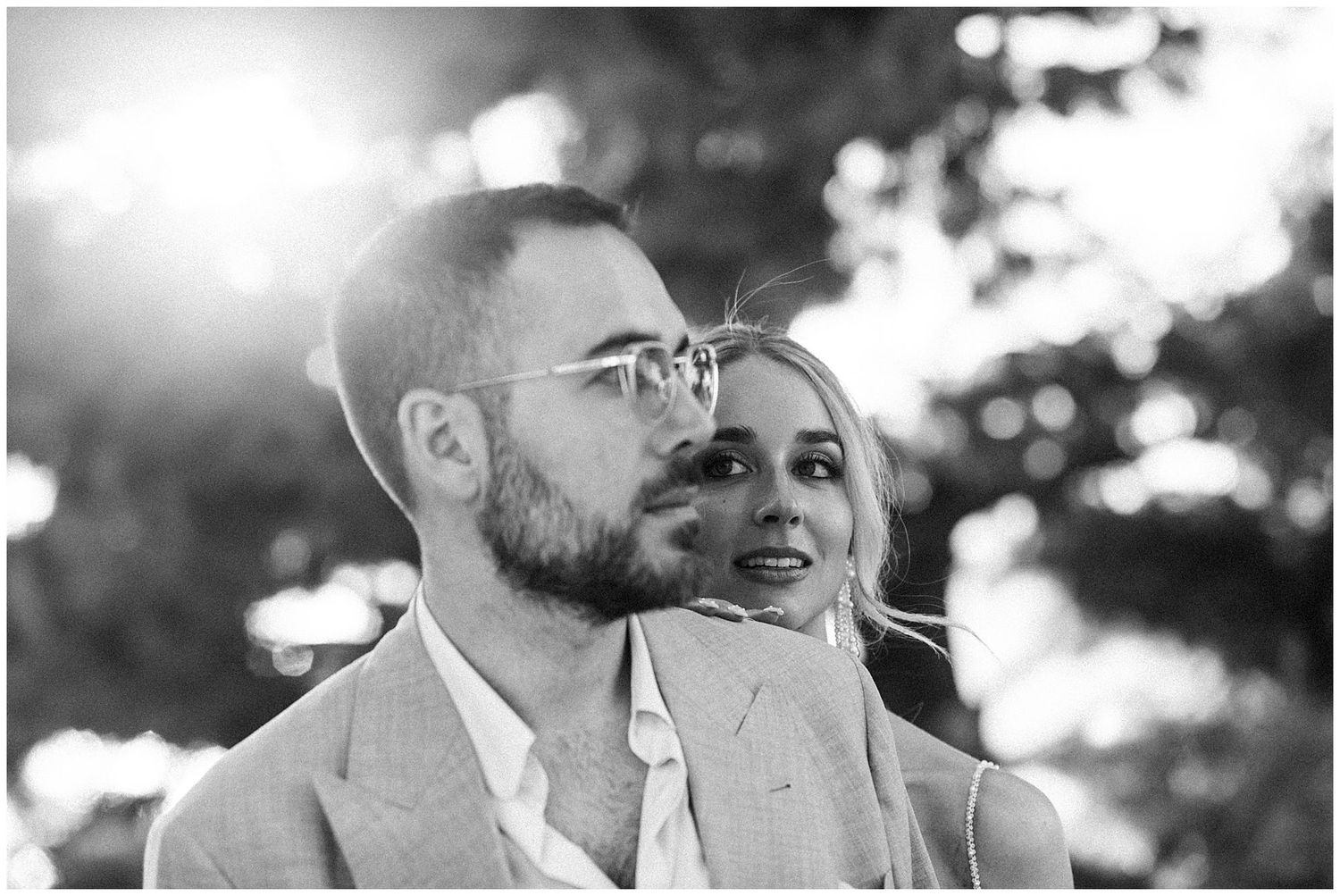 Black and white portrait of a couple in love glances upward together on a sunny outdoor day.