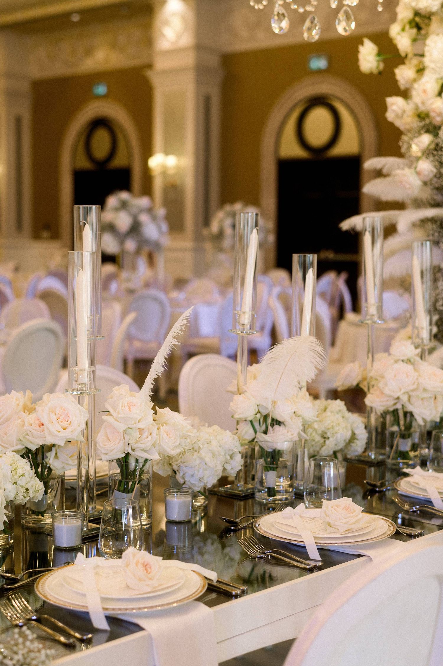 Elegant table setting at a luxurious wedding reception with white flowers, tall glass vases and mirrored decor.