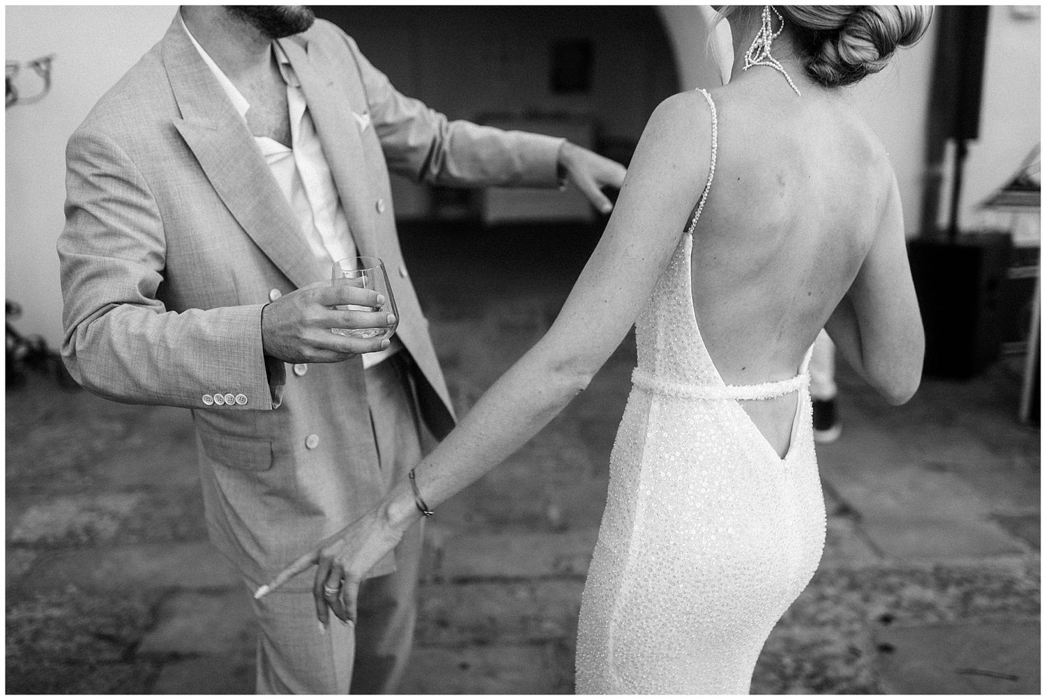 Black and white photo showing a person in a light suit and someone wearing a backless white dress at a social event.