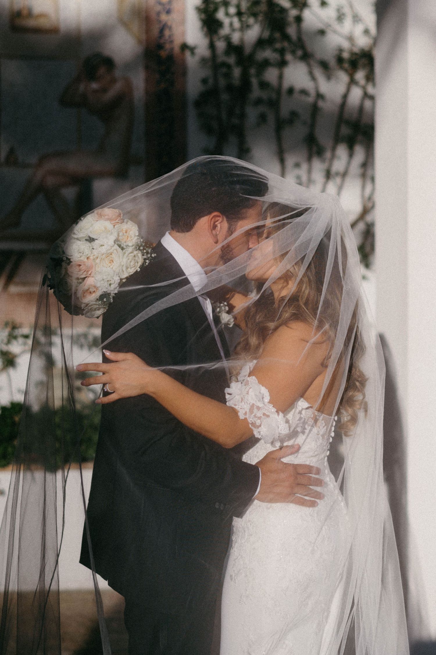 Intimate moment between bride and groom sharing kiss under wedding veil.