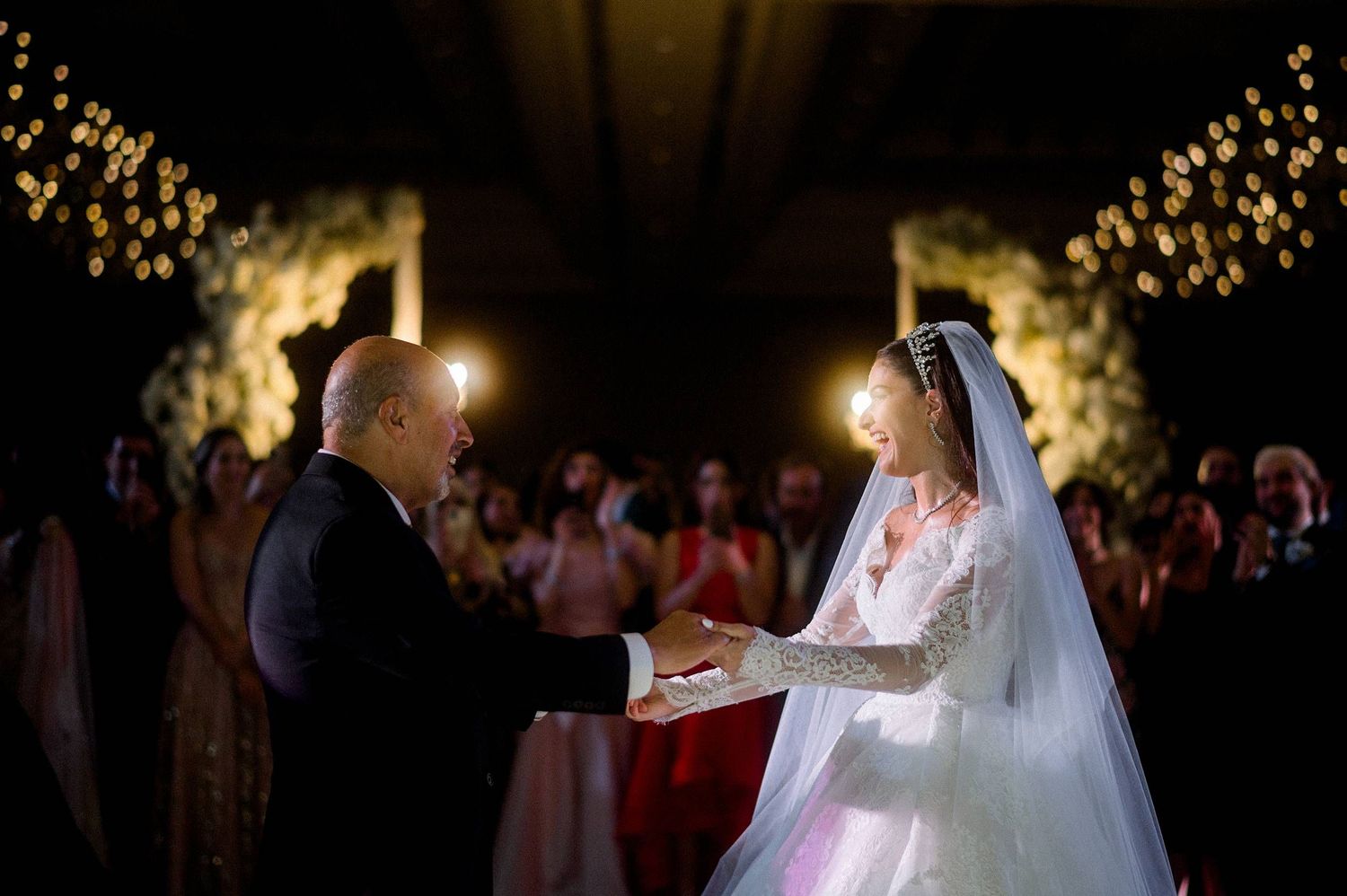 A bride and groom share an intimate moment during their candlelit wedding ceremony with twinkling lights in the background.