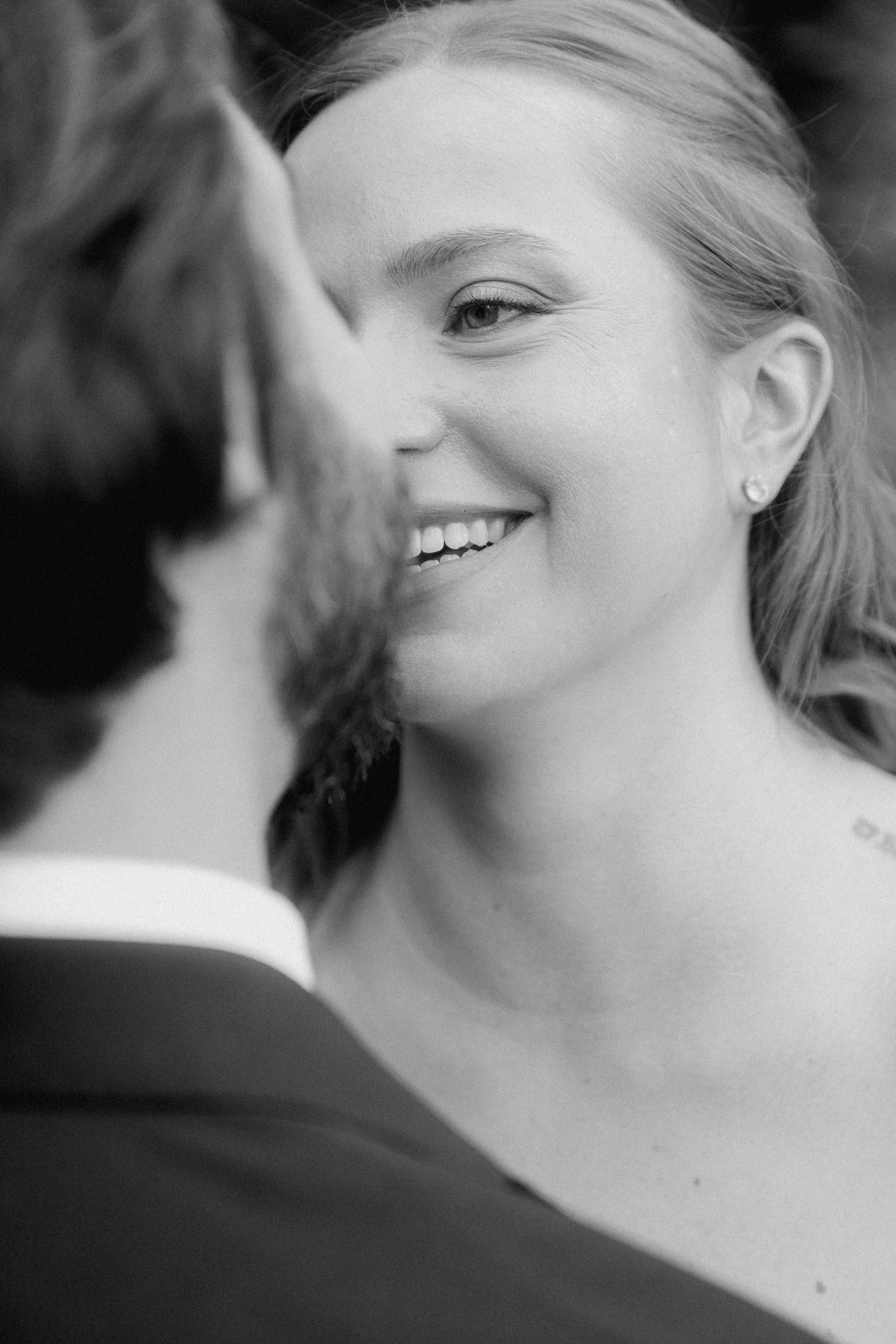 Black and white close-up portrait of a joyful bride smiling at her partner.