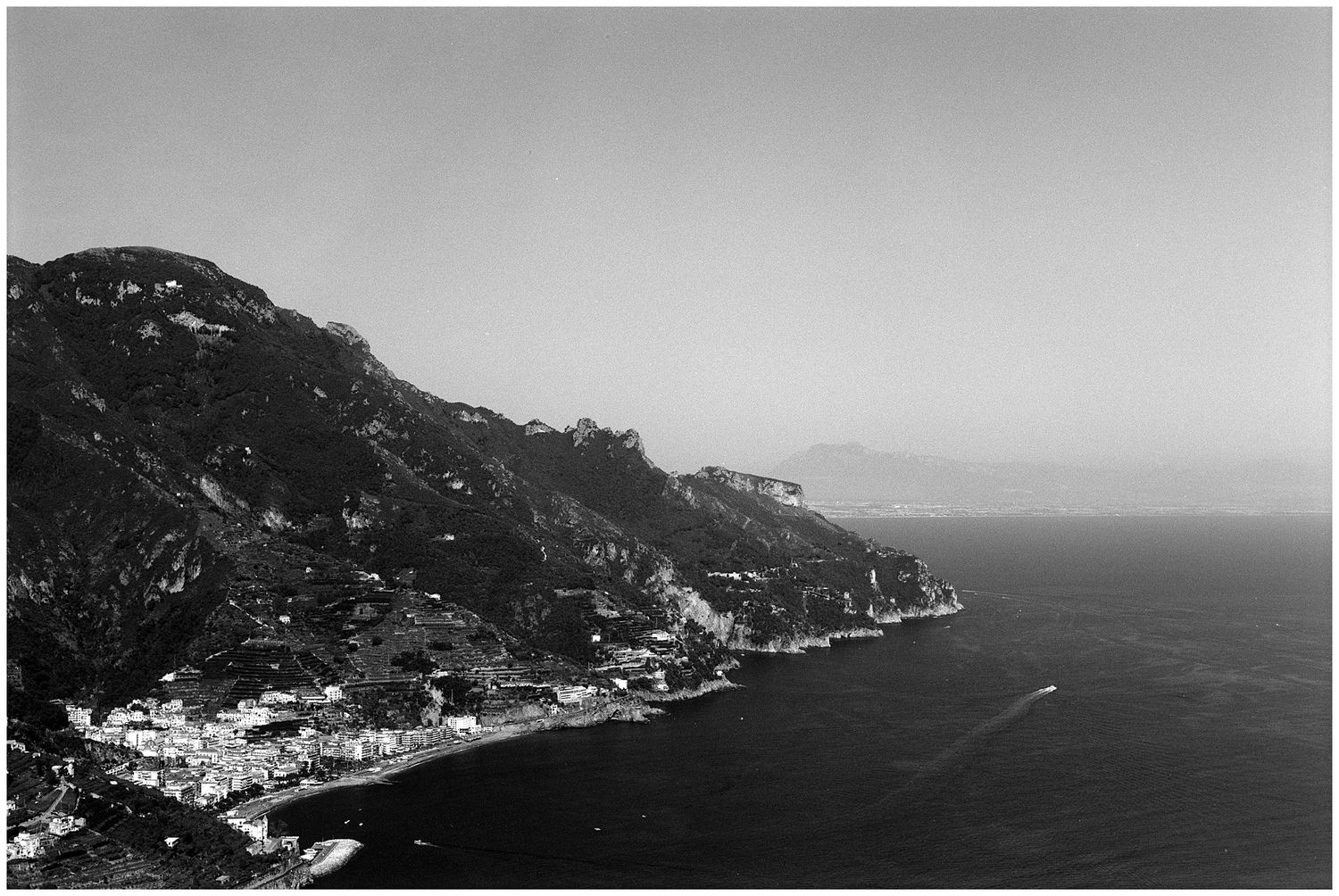 Black and white aerial view of a Mediterranean coastal town nestled between steep cliffs and the sea.