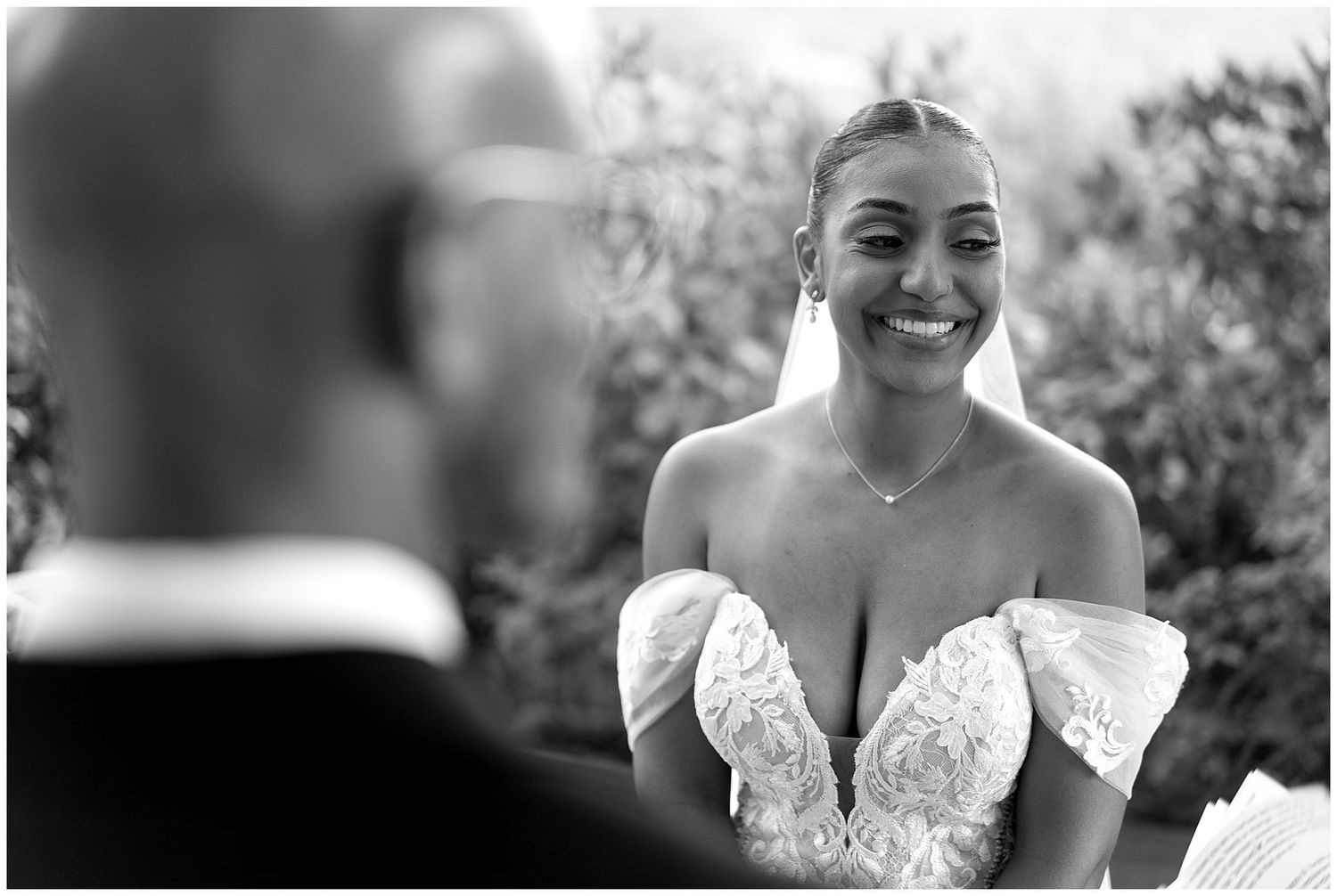 A joyful moment captured in black and white as a bride smiles during her wedding ceremony.