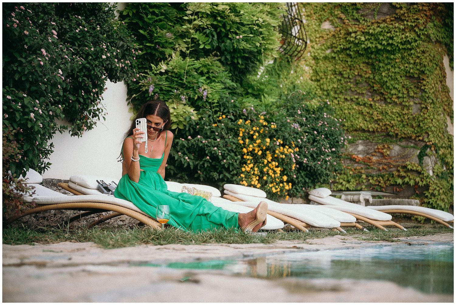Person in green dress relaxing on dock by a pond with wildflowers in summer setting.