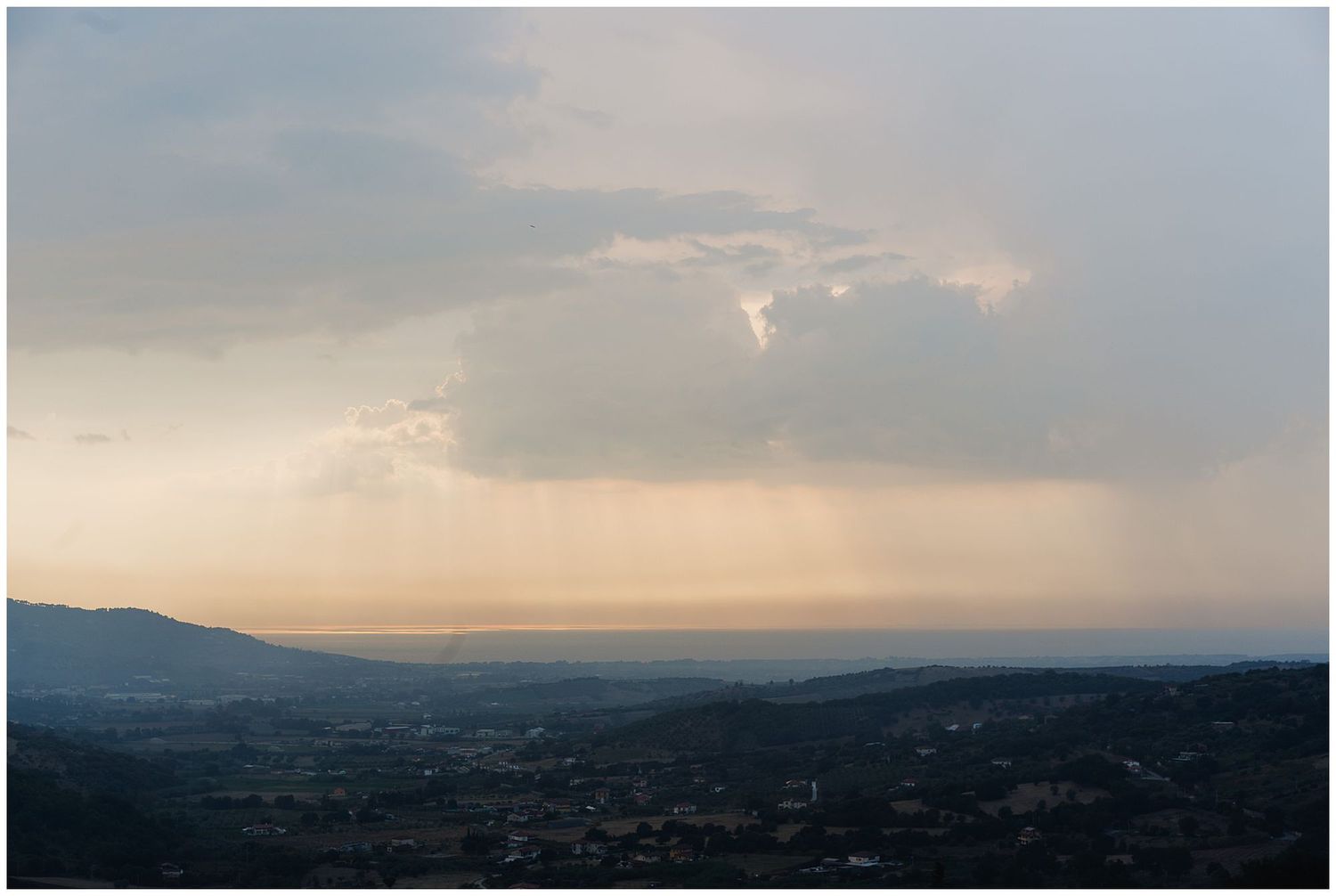 Dramatic sunset sky over rolling hills and valleys with crepuscular rays piercing through cloudy horizon.