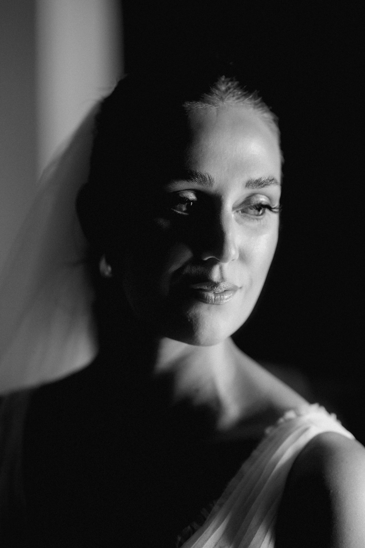 Dramatic black and white portrait with side lighting creating shadows and highlighting facial features in moody contrast.