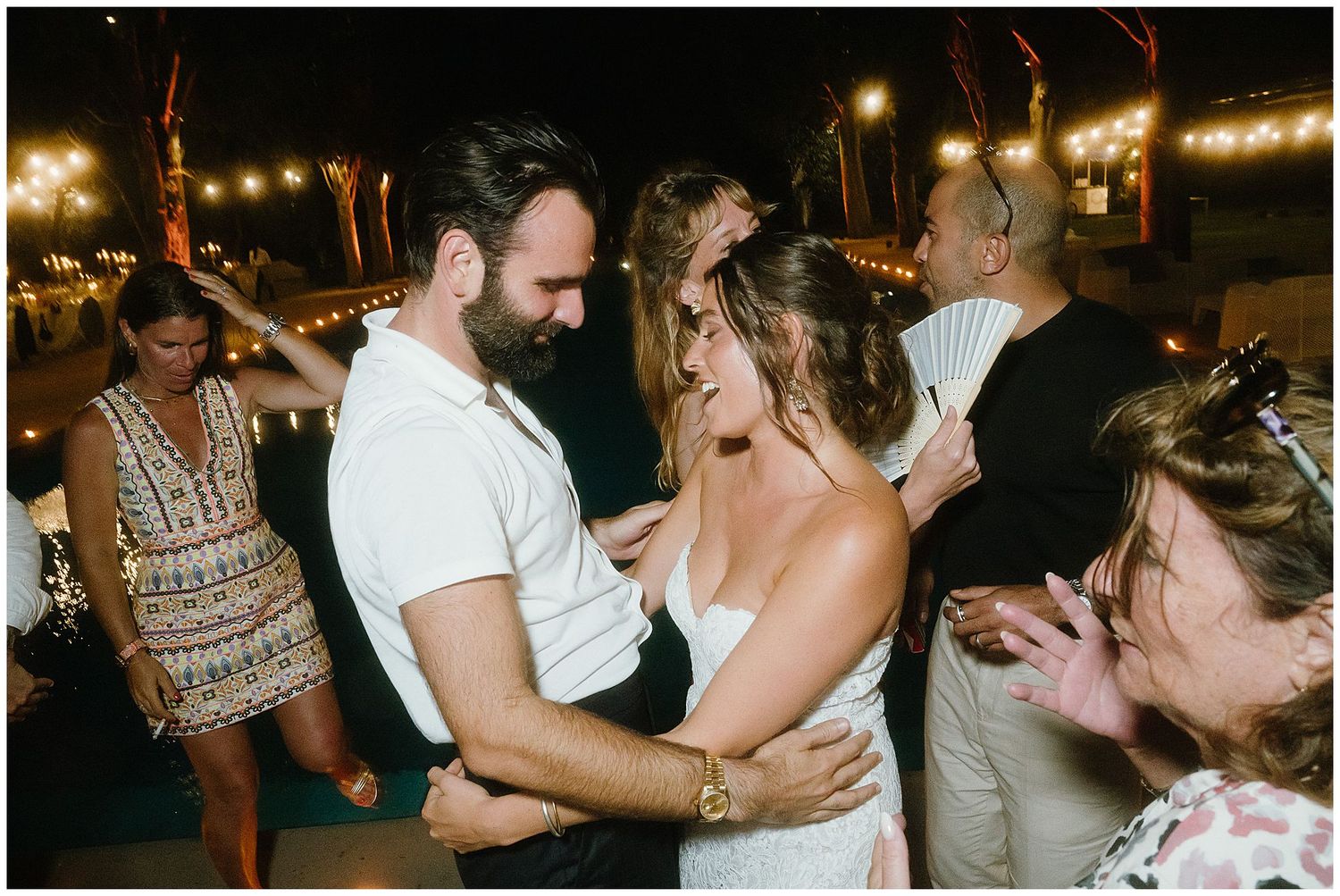 Wedding reception dance party with guests celebrating under outdoor string lights at night.