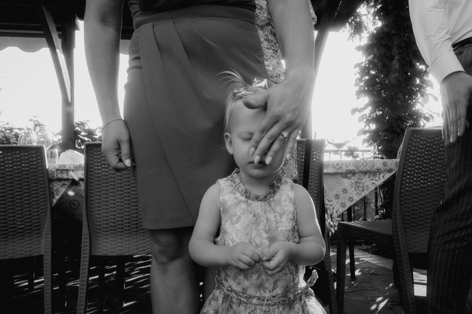A black and white image of a parent and child standing together on a patio with wicker furniture visible.