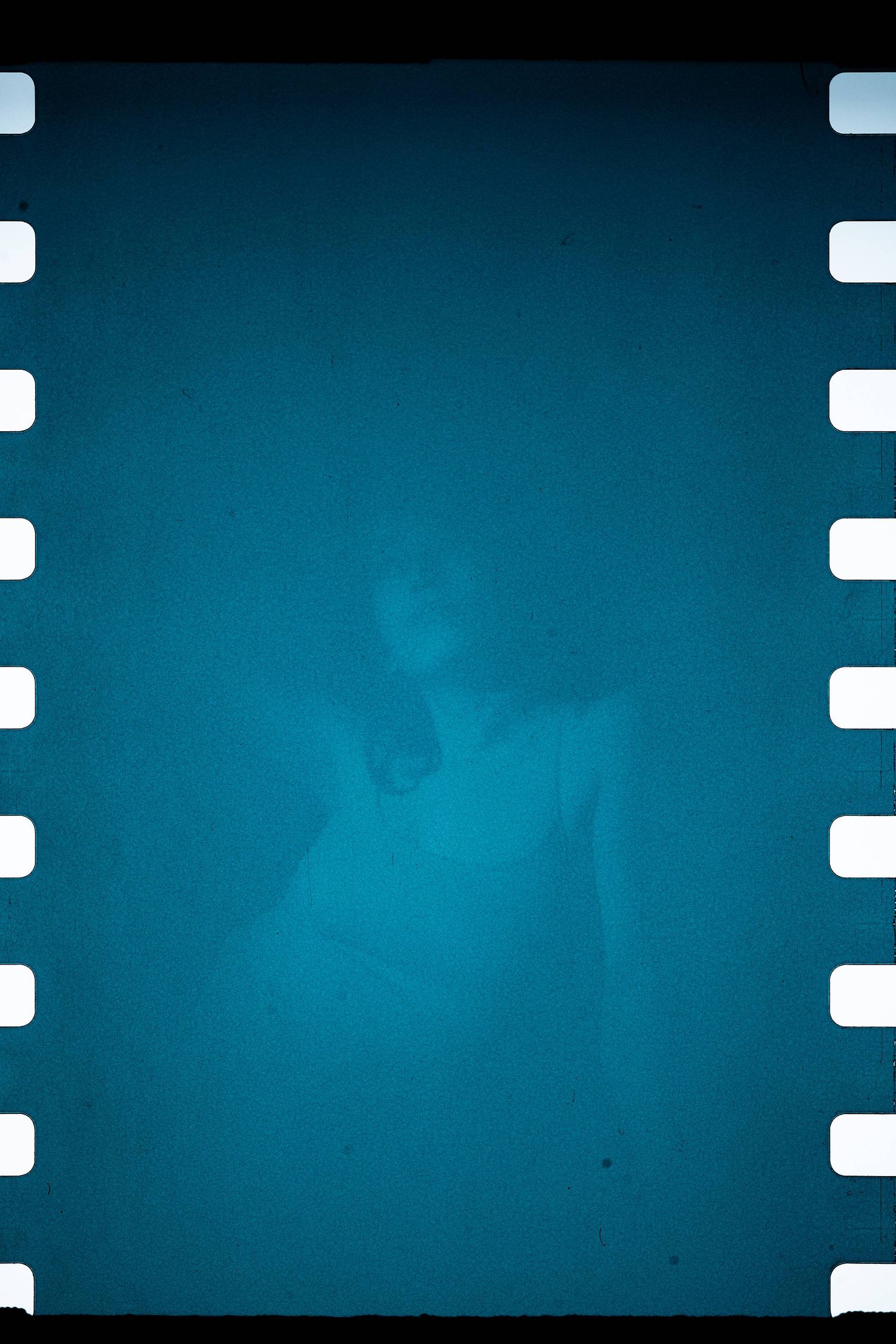 Experimental film frame showing dark turquoise underwater effect with sprocket holes along edges.