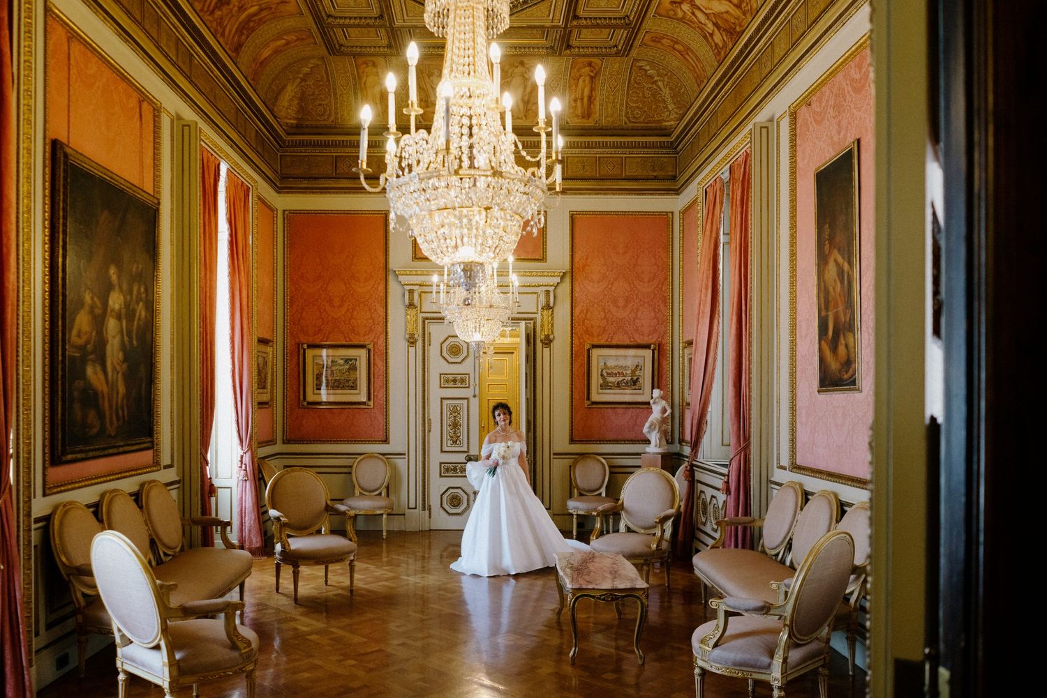 Ornate ballroom with crystal chandeliers and red walls featuring antique furniture and classical decor.
