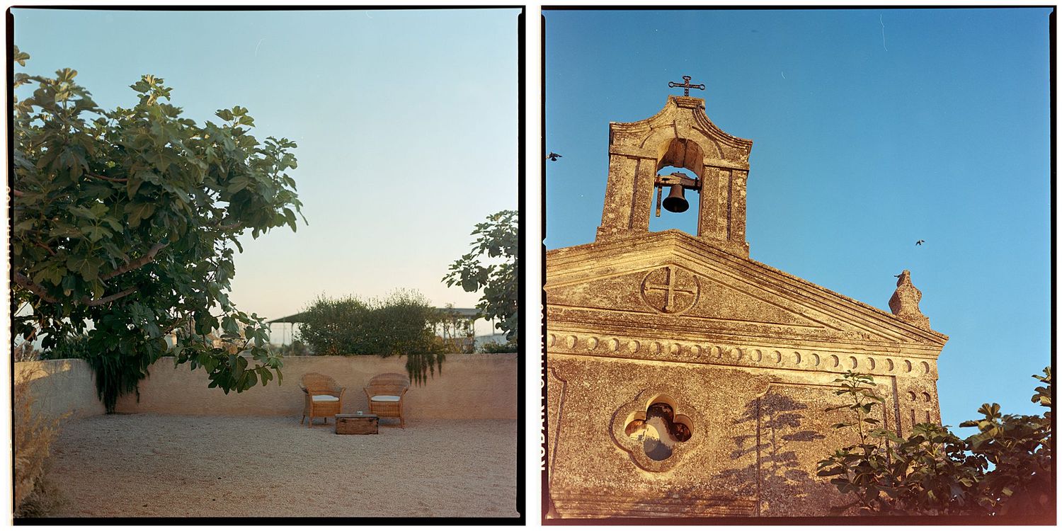 Rustic stone church with bell tower beside peaceful courtyard with benches under tree.