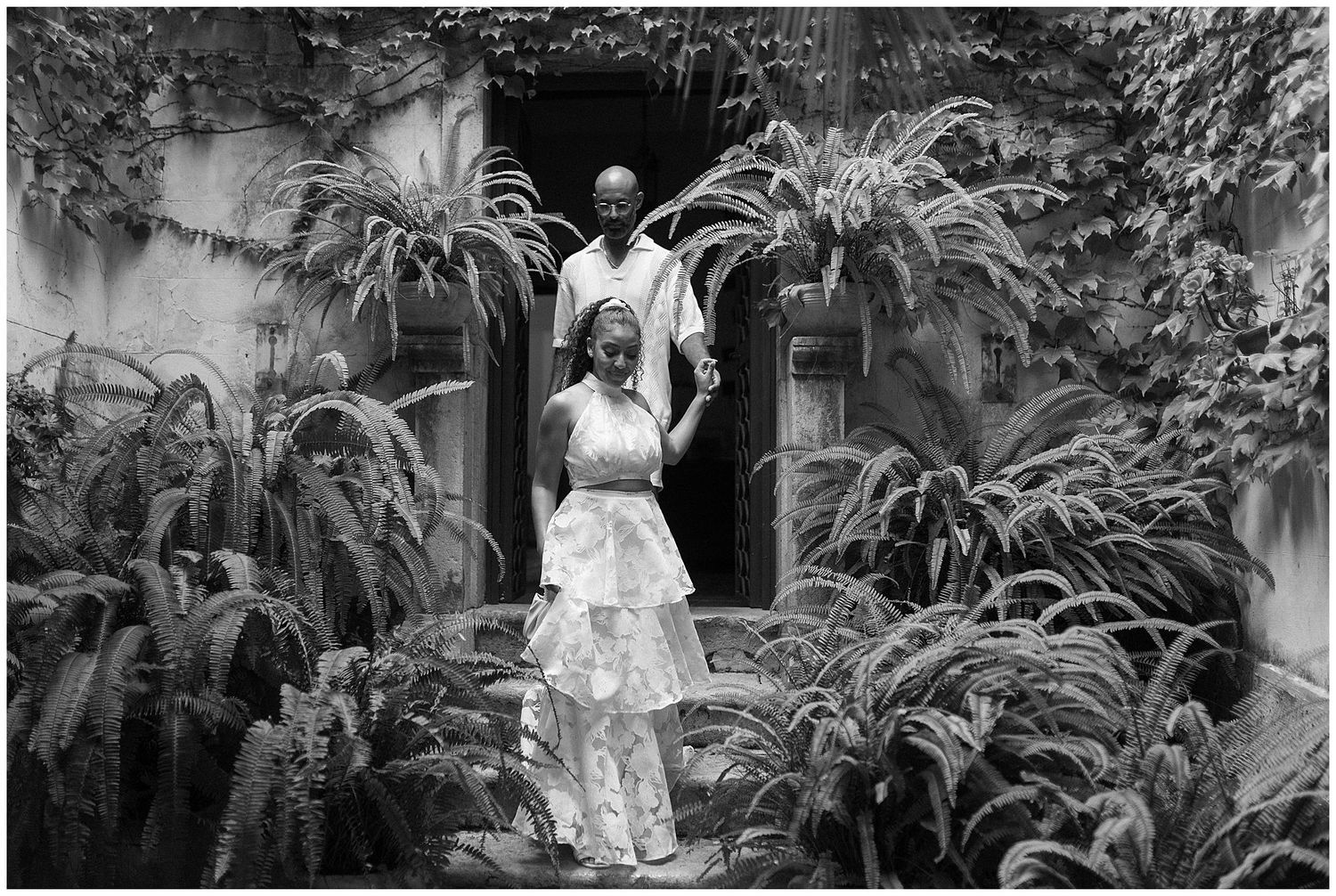 A black and white bridal portrait surrounded by lush ferns and plants in a garden setting.