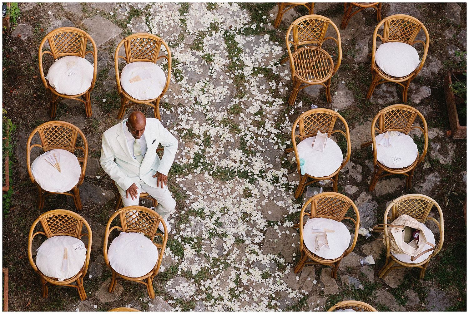 Rustic woven rattan chairs arranged in rows on a gravel pathway with white cherry blossom petals scattered around.