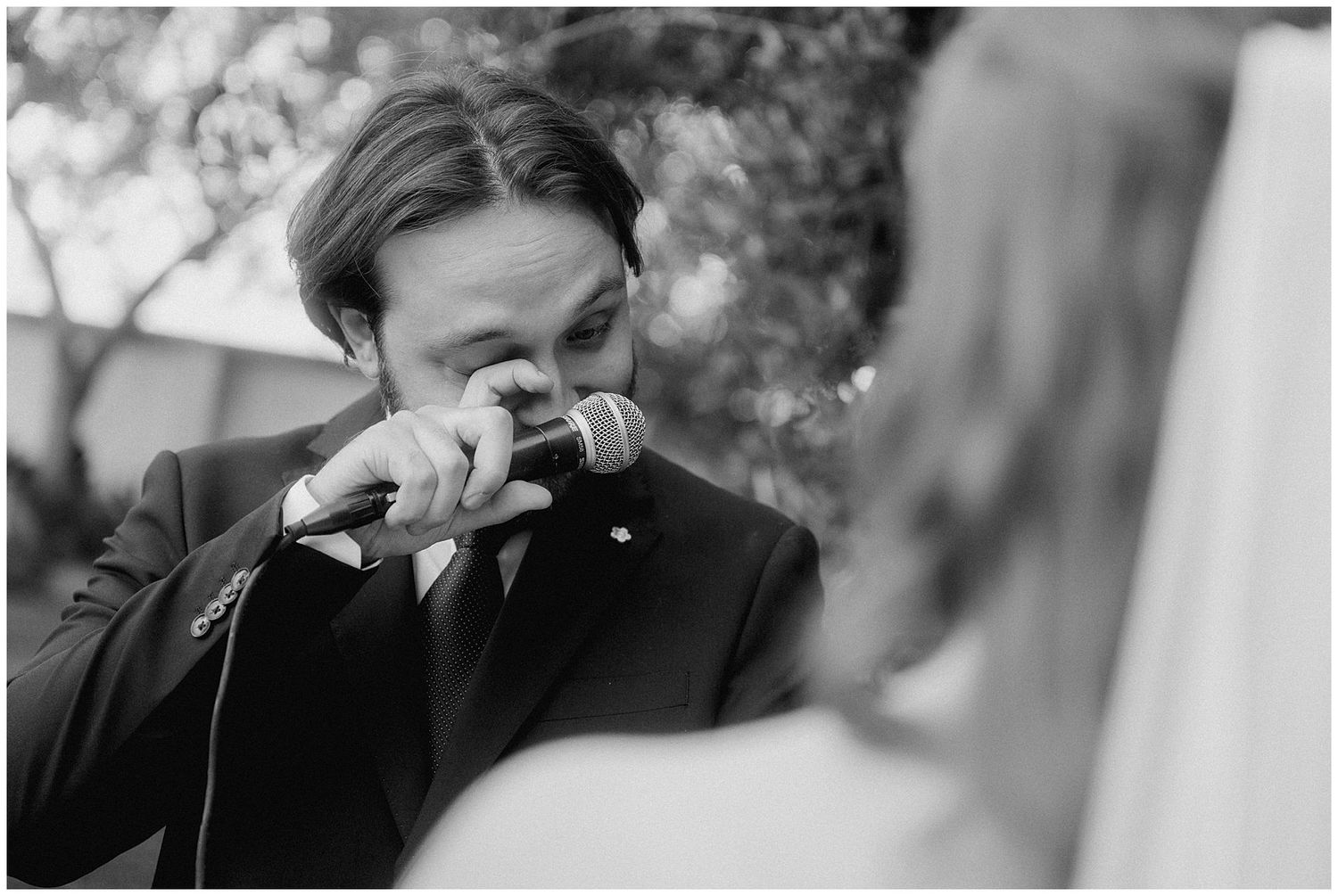 Black and white photo of someone looking down while holding a tissue to their face during an emotional outdoor moment.