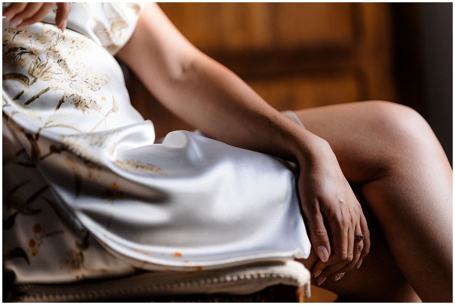 A person relaxes on a vintage chair wearing a white silk dress that drapes elegantly over their legs.