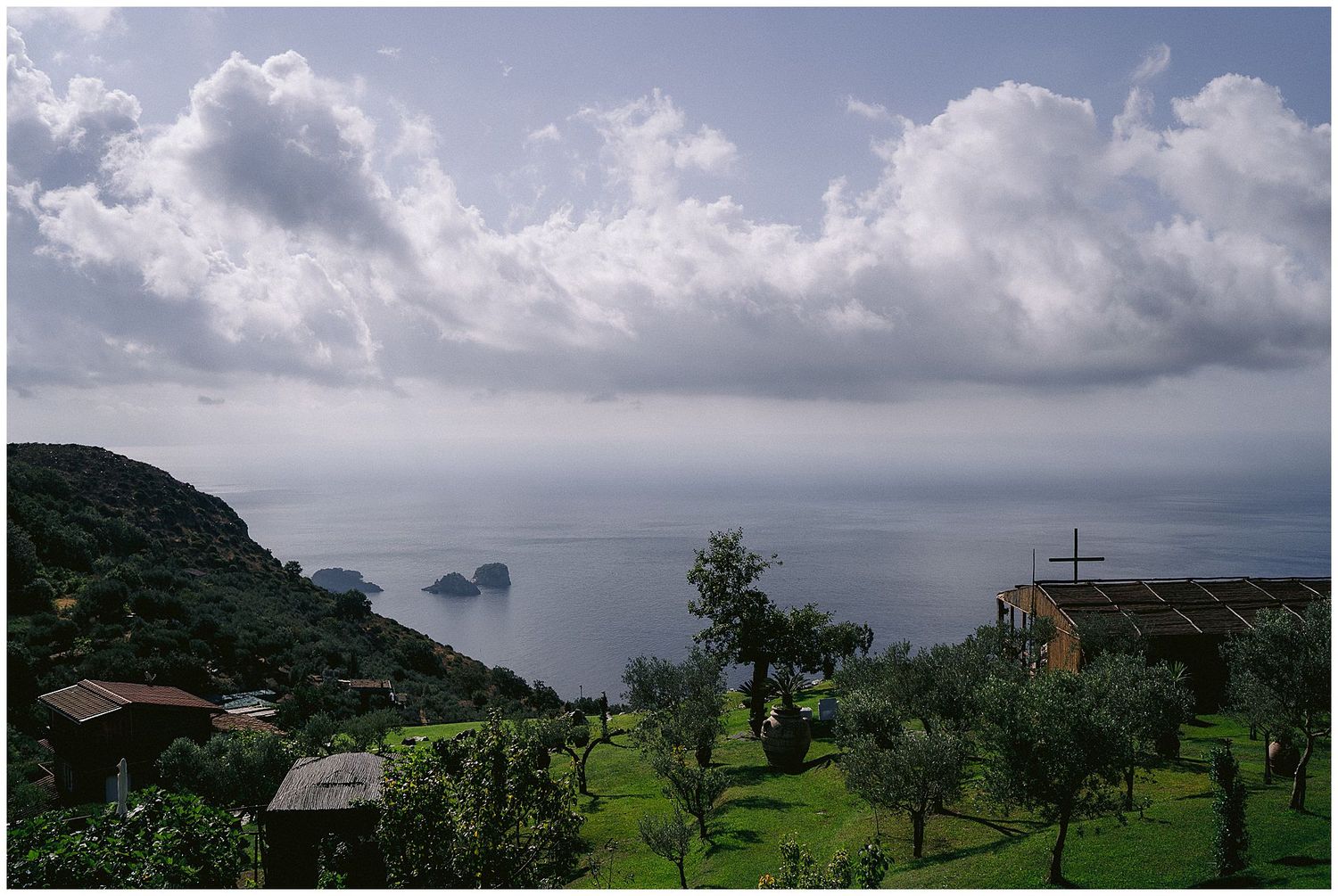 A lush green hillside overlooking the ocean with small islands in the distance and dramatic clouds in the sky.