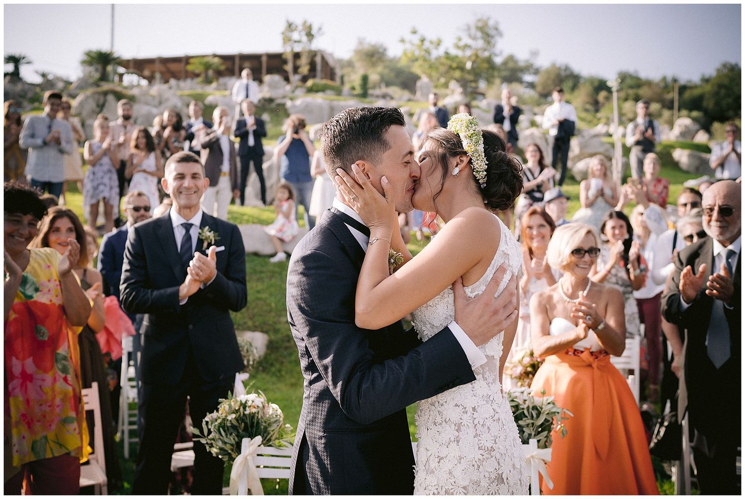 Guests at an outdoor wedding ceremony celebrate and take photos of the happy couple on a sunny day.