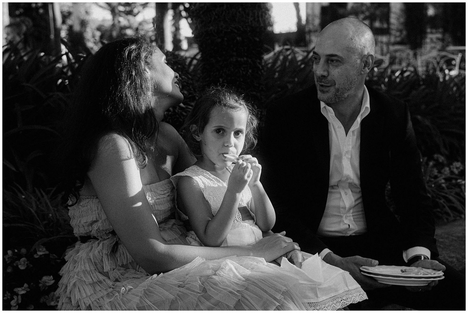 A black and white photograph shows three elegantly dressed people at a formal dinner gathering.