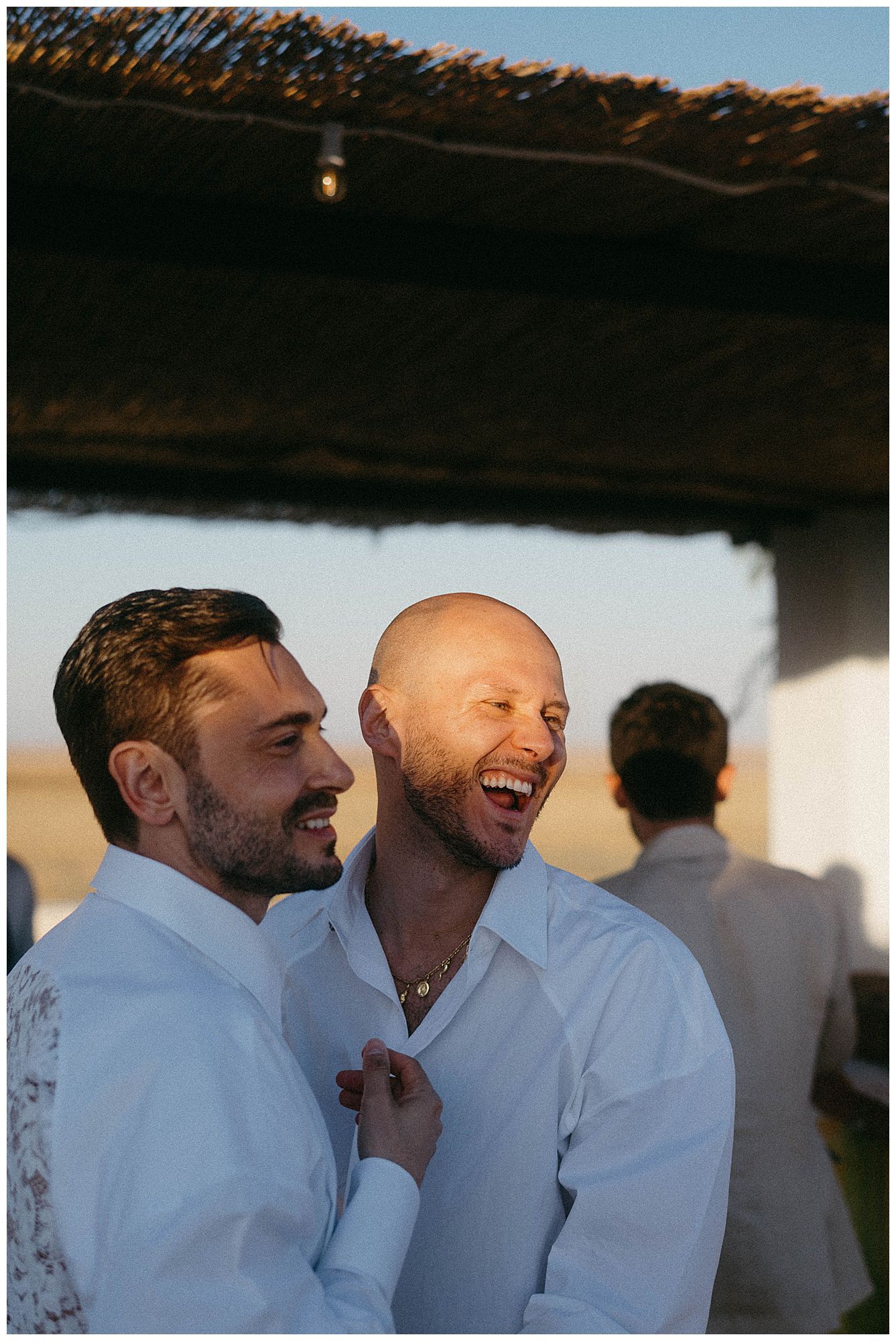 Two people in white button-down shirts share a joyful laugh together at an outdoor gathering.