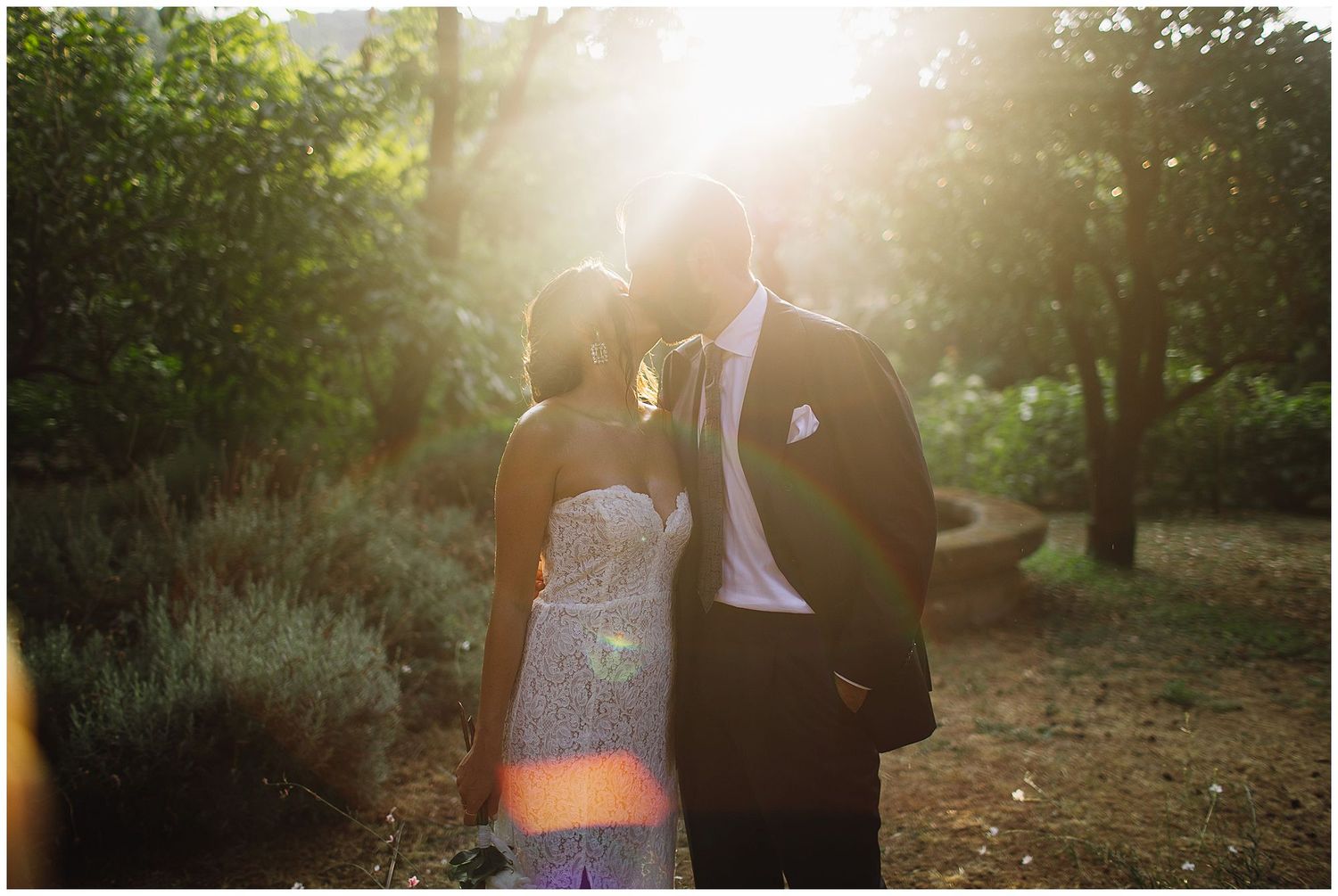 A couple shares an intimate moment in a sun-drenched garden setting with beautiful lens flare effects.