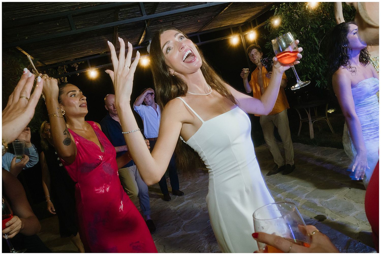 A wedding celebration showing joyful dancing under string lights with people in formal attire.