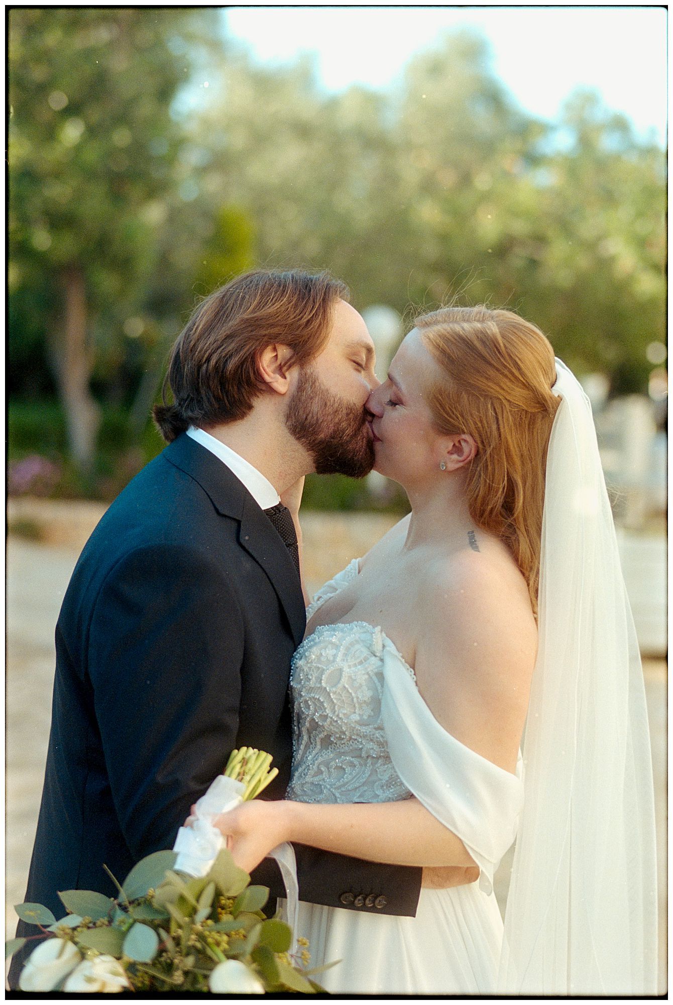 A romantic outdoor wedding photo showing a couple sharing their first kiss as newlyweds in their formal attire.