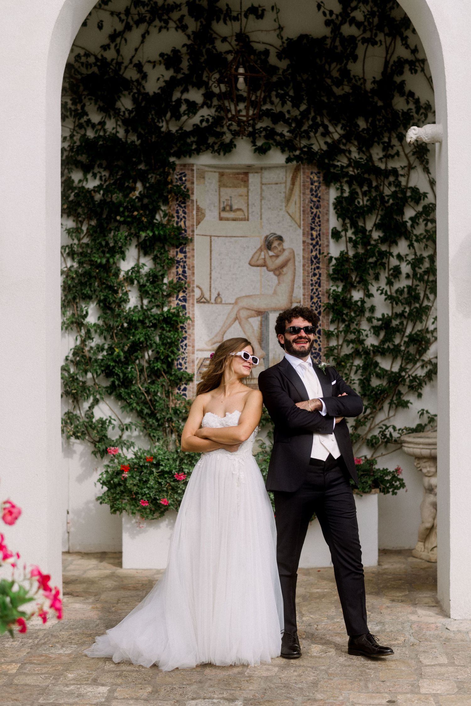 Stylish couple posing under ivy-covered archway at elegant wedding venue.
