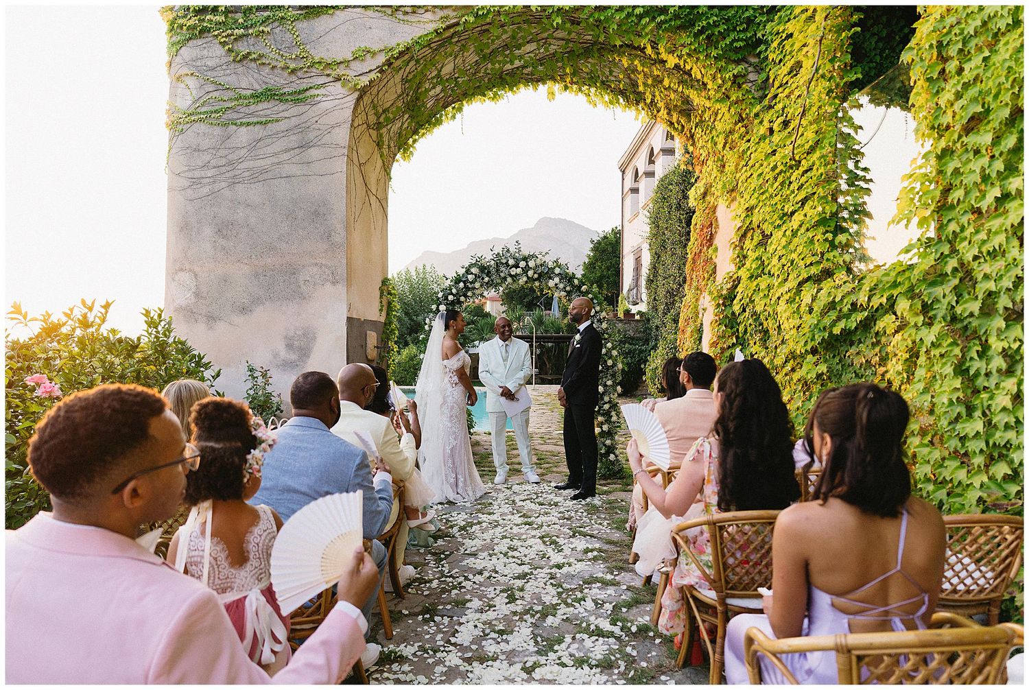 Wedding guests gathered in a stone archway during an outdoor reception at dusk.