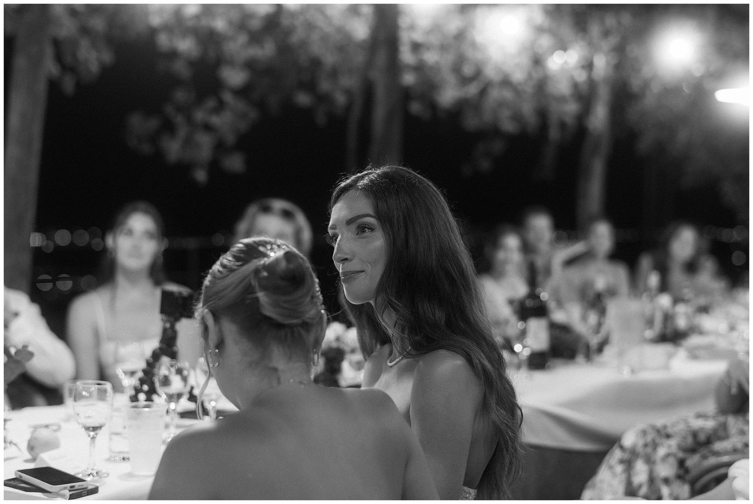 Black and white photo of guests having an animated conversation at an outdoor evening wedding reception.