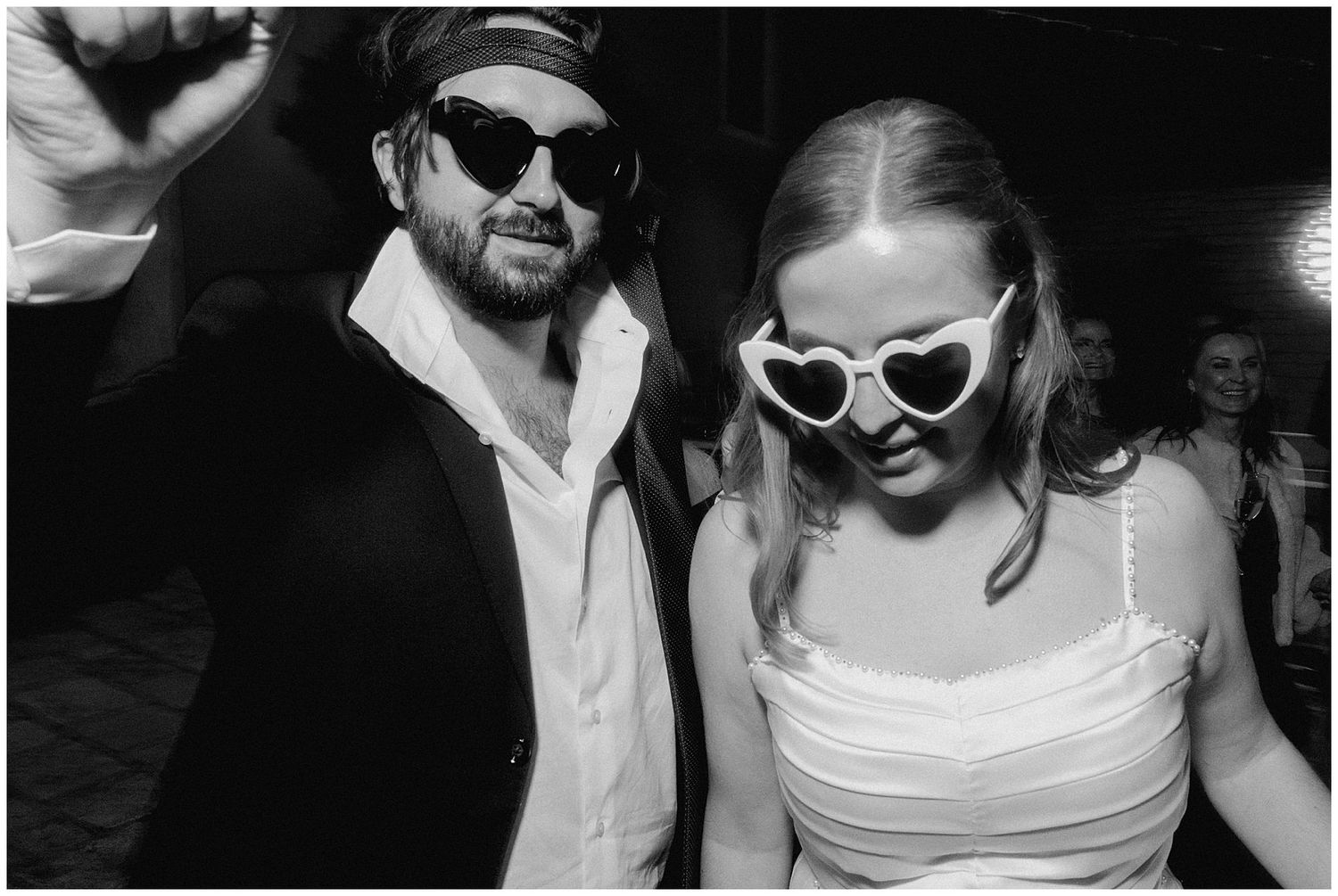 Black and white photo showing a couple in retro sunglasses at a festive celebration together.