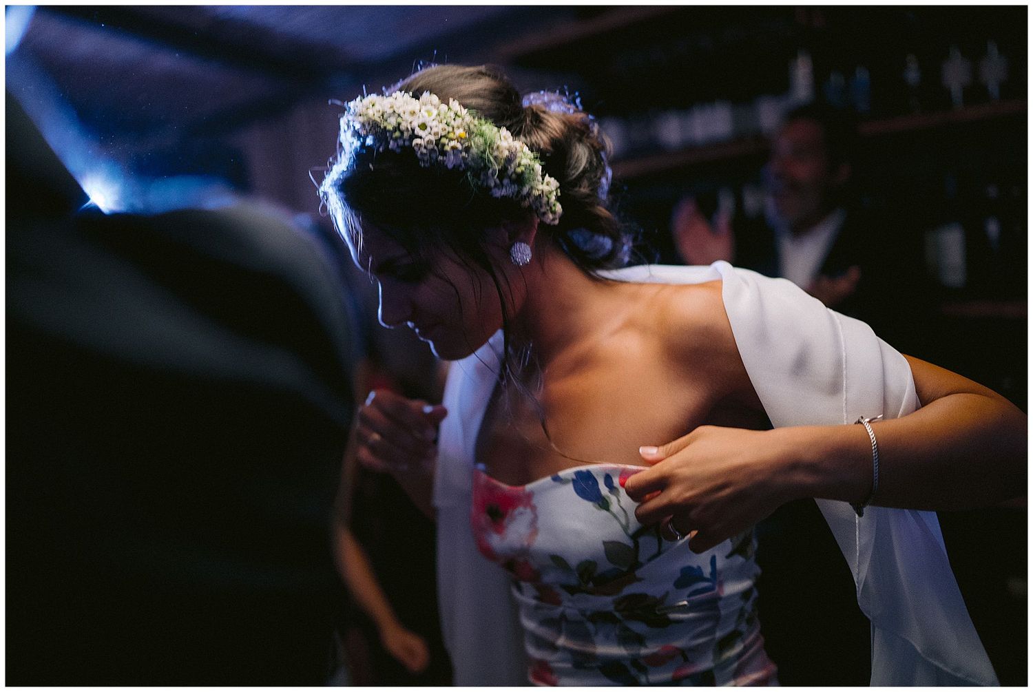 A person in a floral dress and white shawl dances at an evening celebration wearing a delicate flower crown.