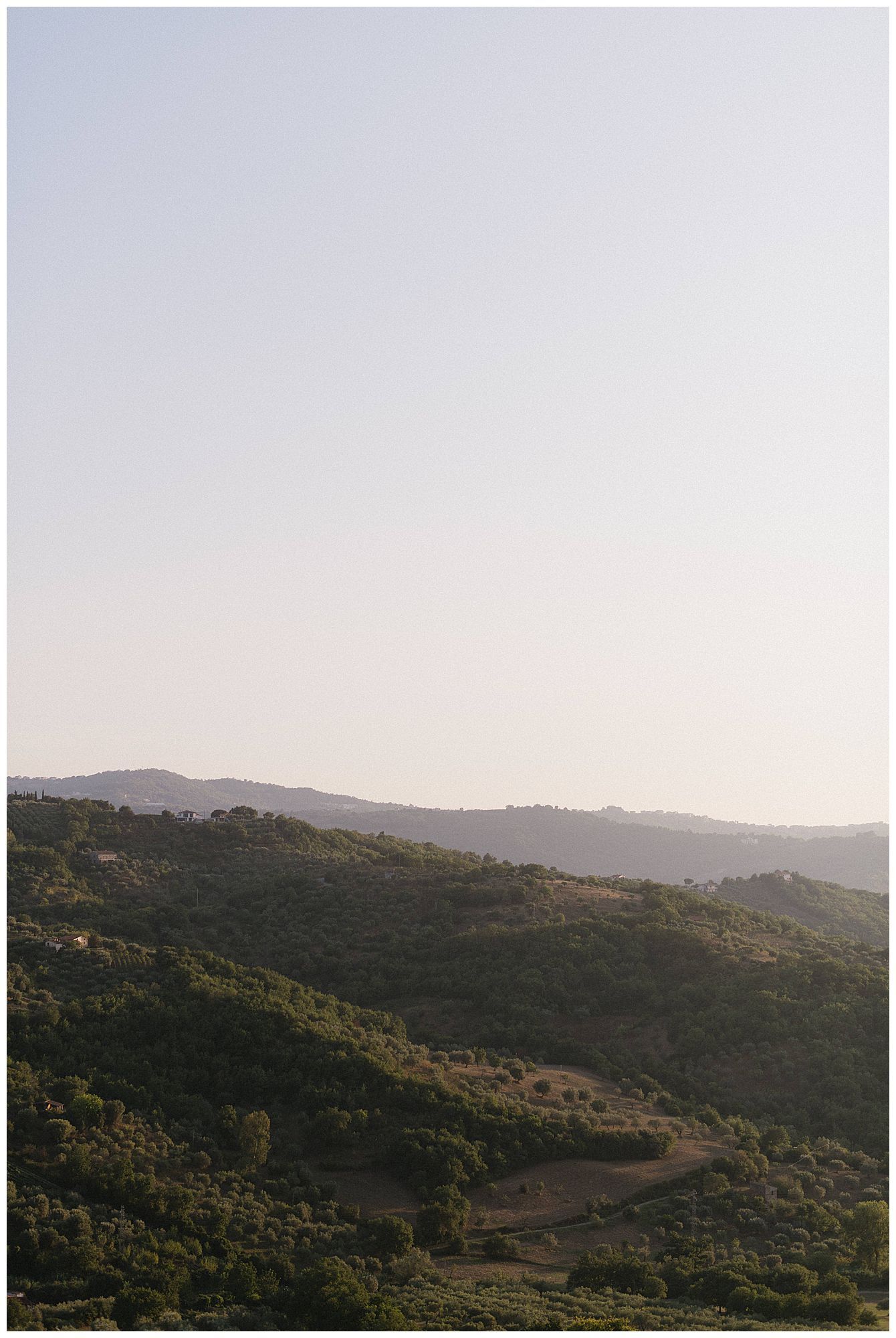 Rolling hillside landscape at sunset with mountains in the distance and lush green vegetation.