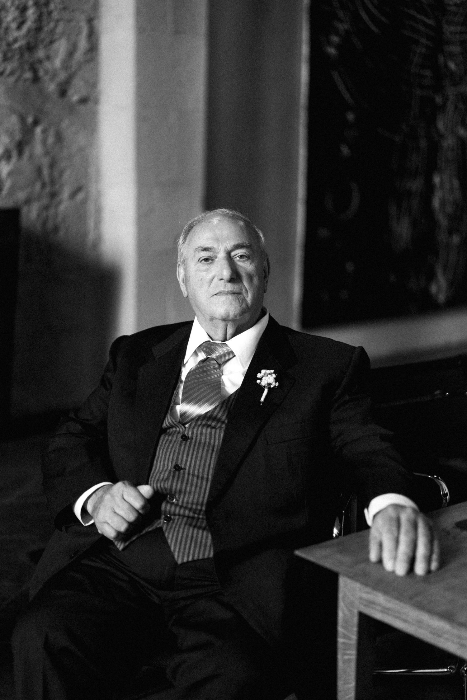 A formal portrait of someone wearing a pinstripe suit with a boutonniere in a dimly lit room.