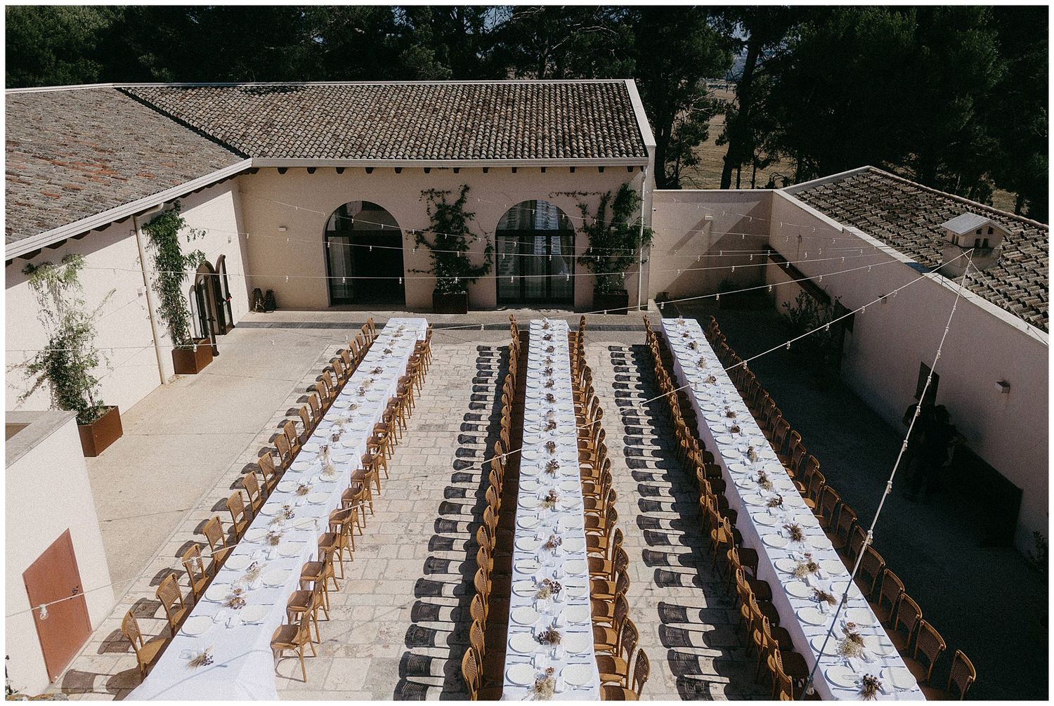 Overhead view of elegant outdoor wedding reception setup with long tables and arched Spanish architecture in a courtyard.