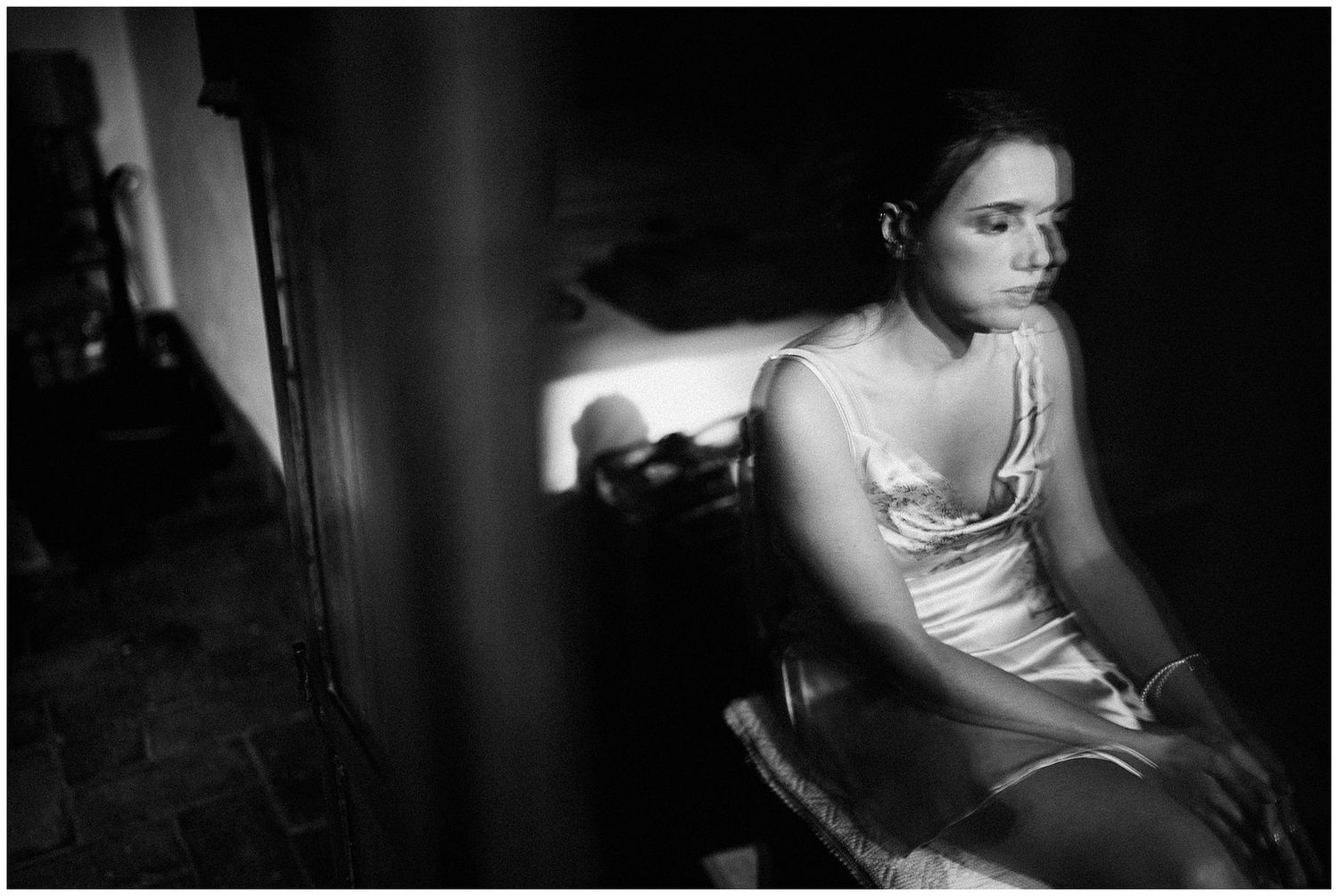 Dramatic black and white photograph showing a person in evening wear seated in dark moody lighting.