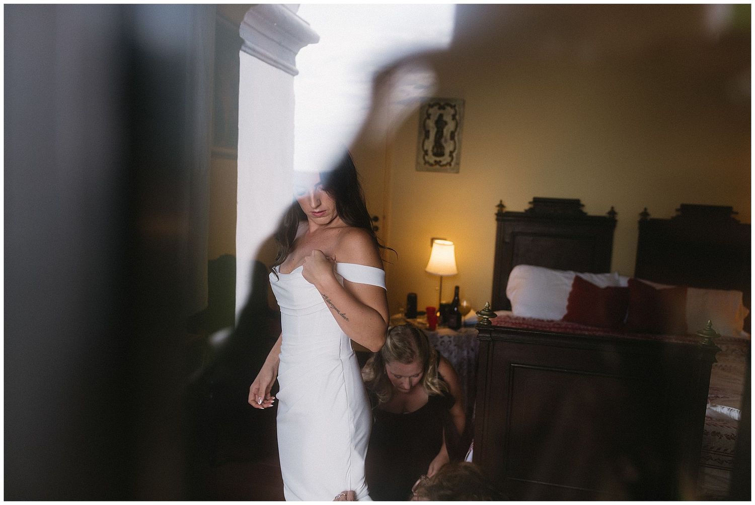 A person in a white dress getting ready in a bedroom with a lamp casting warm lighting.