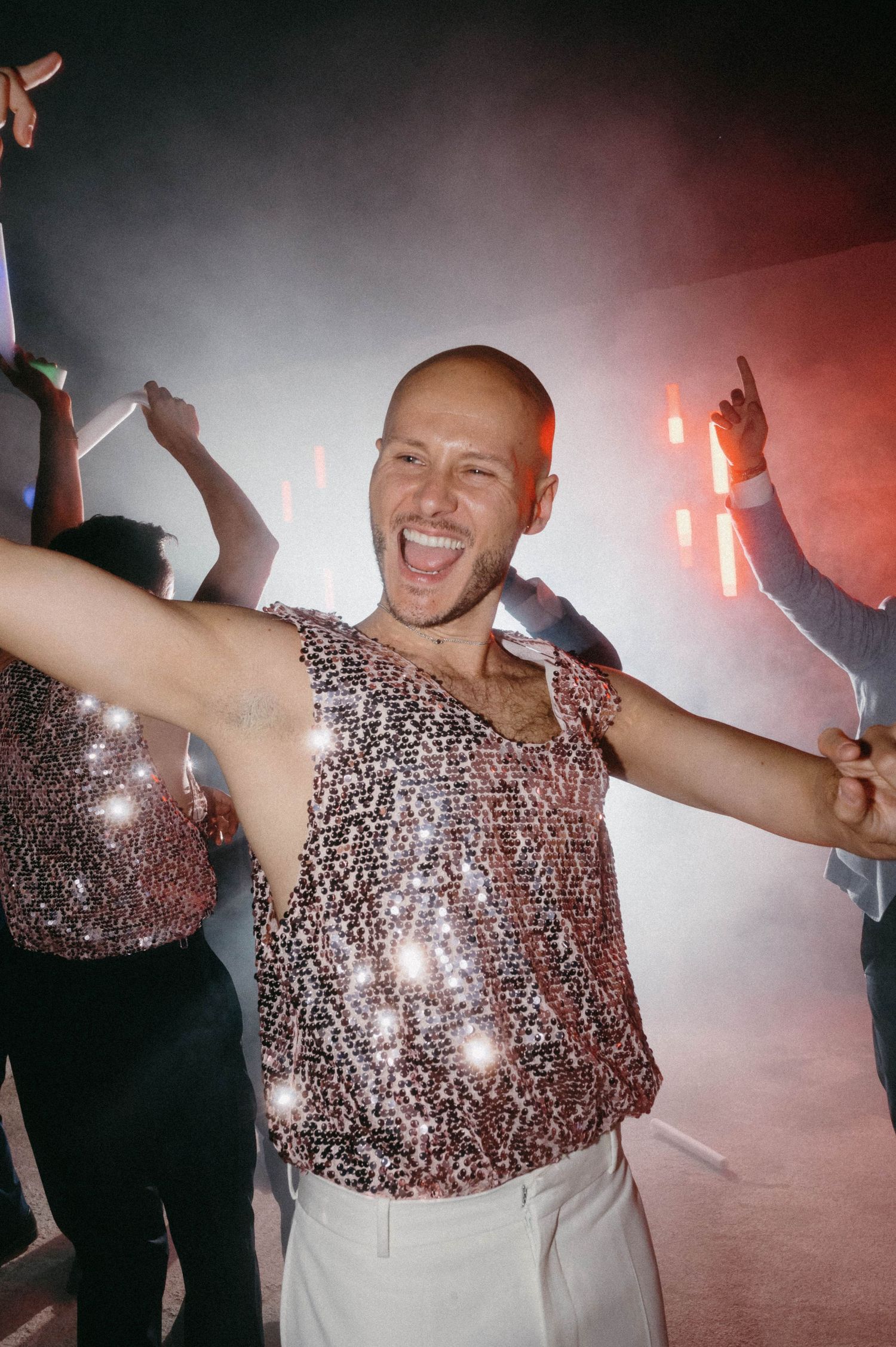 A person dances joyfully in a sparkly sequined top at a nightclub with atmospheric lighting.