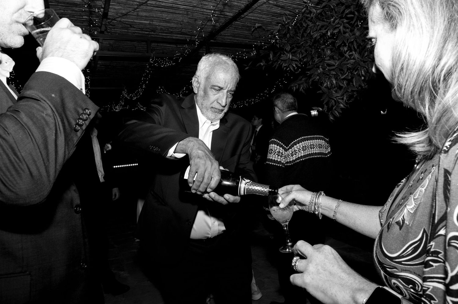 A vintage black and white photo shows people exchanging drink pours or toasts at what appears to be a social gathering.