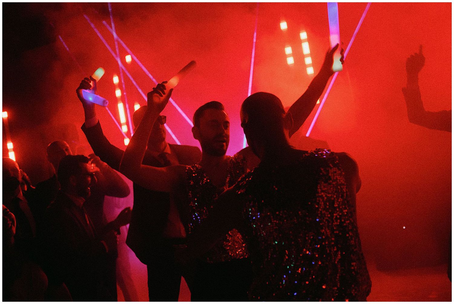 Silhouetted figures dancing with glowsticks in a red-lit nightclub atmosphere.