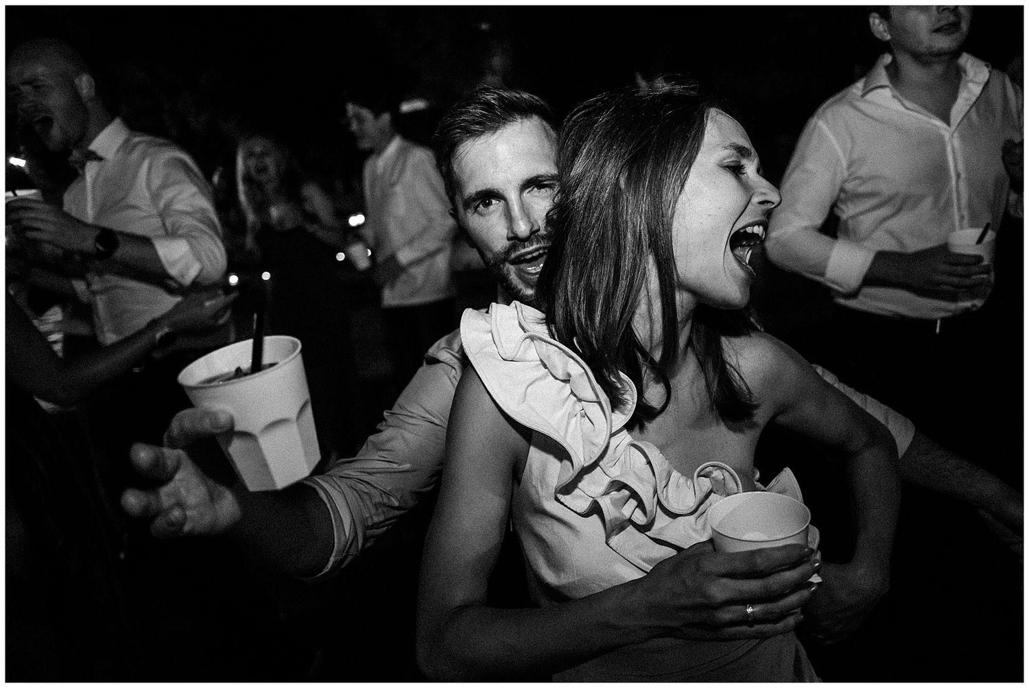 Black and white photo of people dancing and celebrating at a nightclub or party among a crowd.