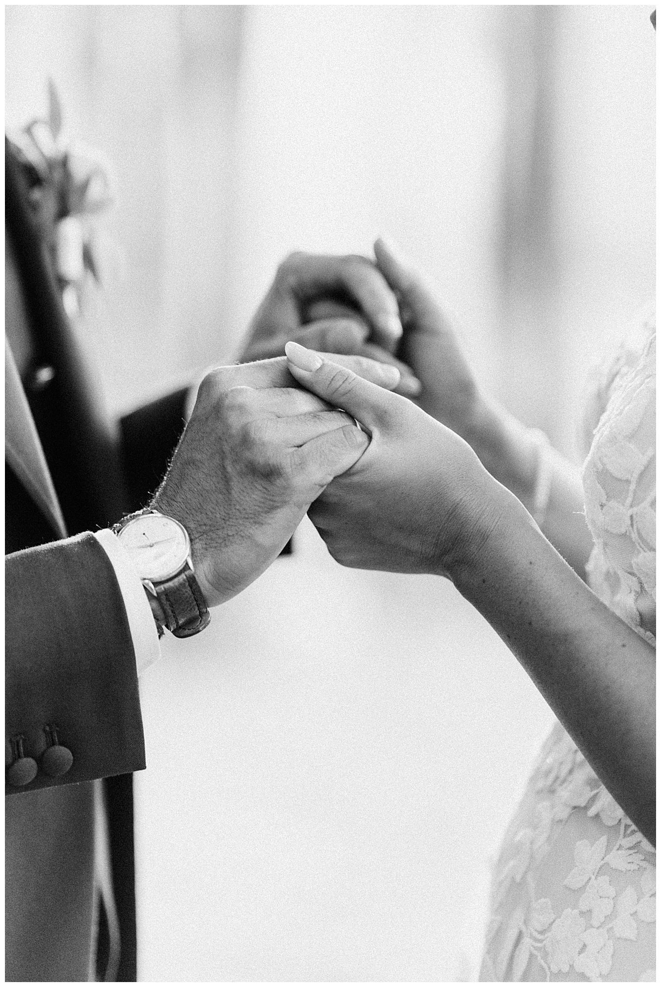 Black and white close-up of hands exchanging wedding rings during a marriage ceremony.