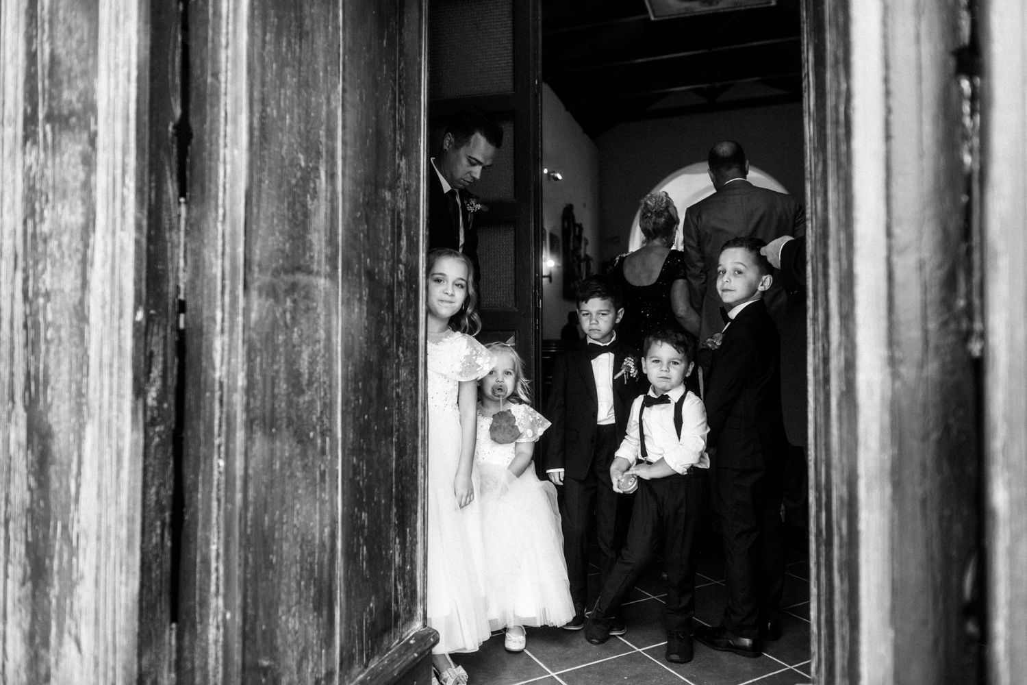 Wedding party gathered in rustic doorway for black and white photograph.