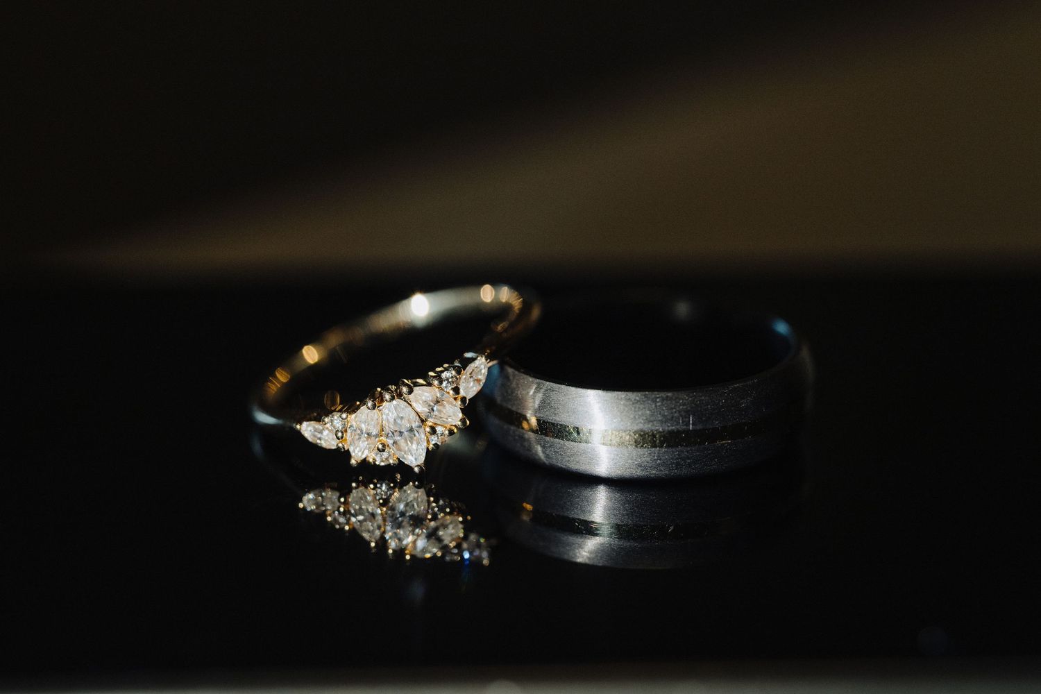 Wedding rings photographed with dramatic lighting on dark reflective surface.