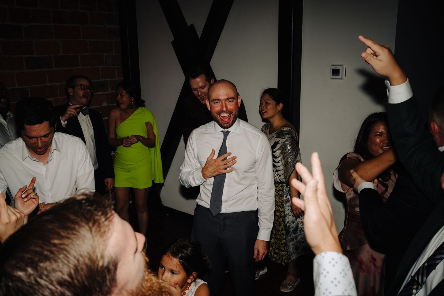 Wedding reception guests dancing and celebrating with hands raised in the air.
