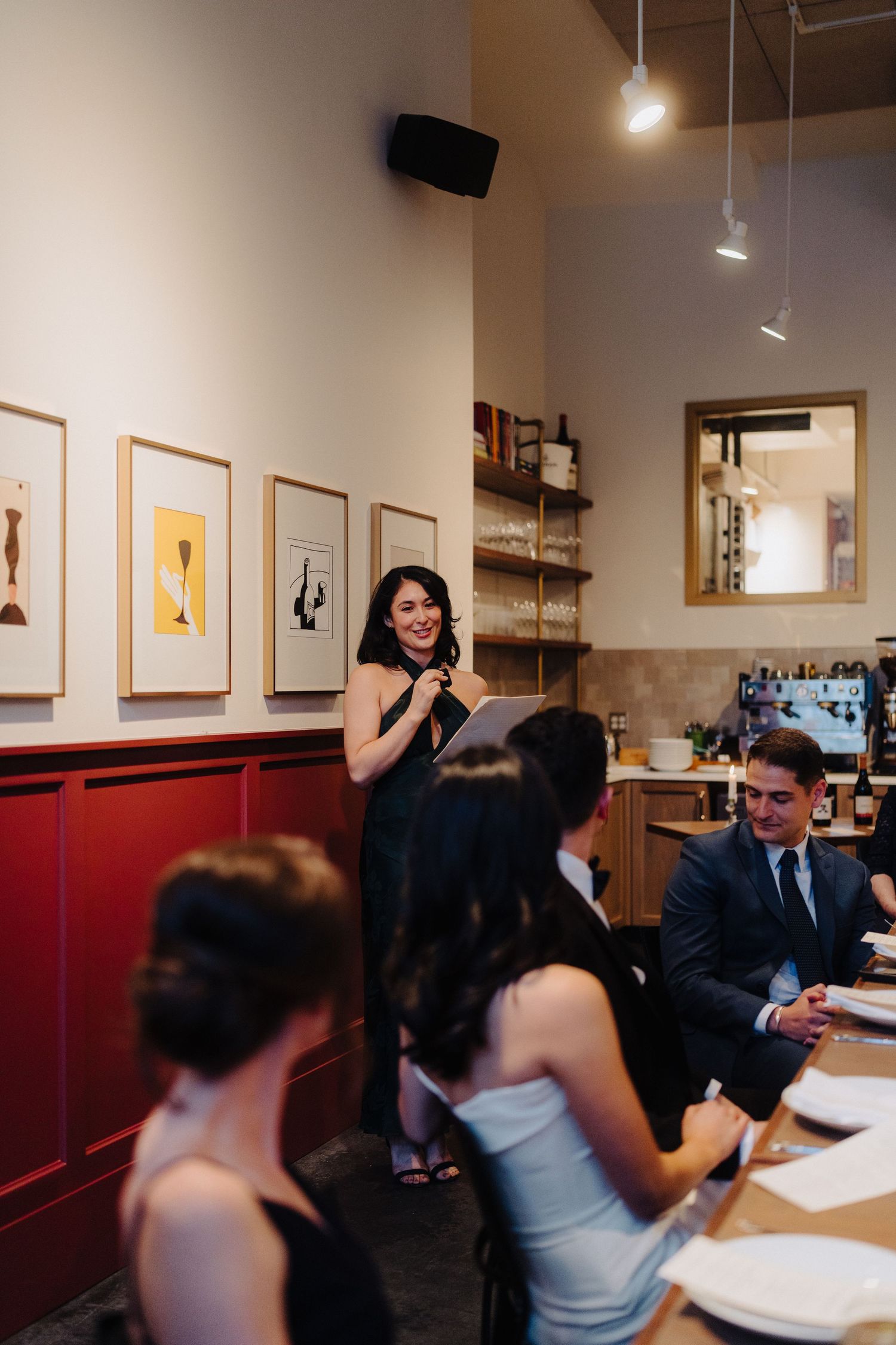 A reception speech being given in a cozy restaurant with red walls and framed artwork.