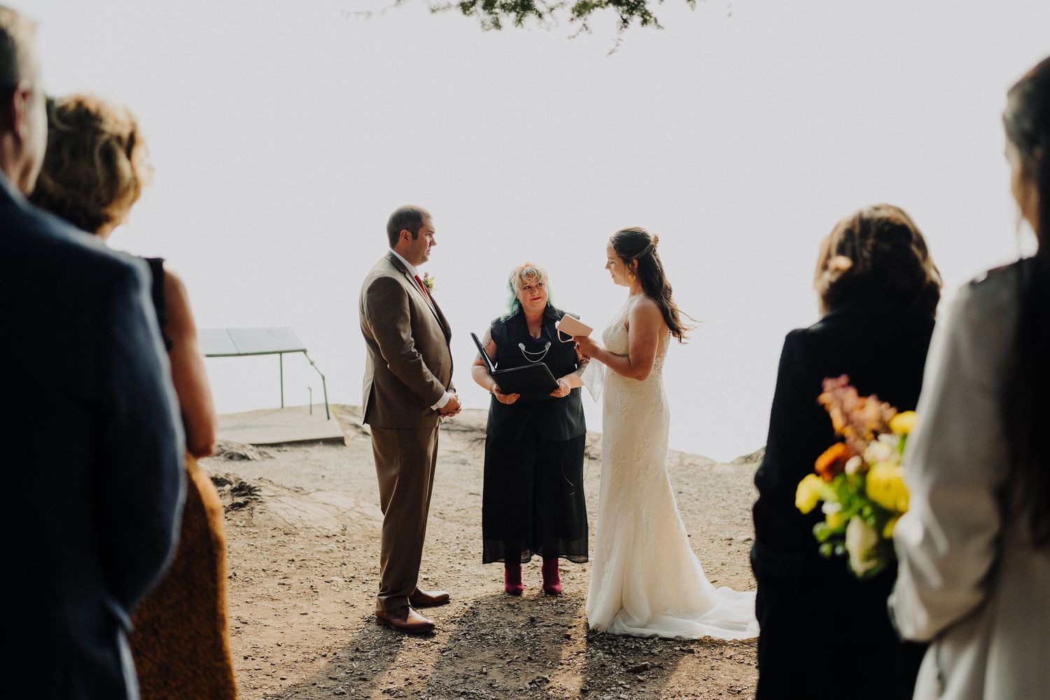 Intimate outdoor wedding ceremony taking place at a scenic overlook on a bright day.