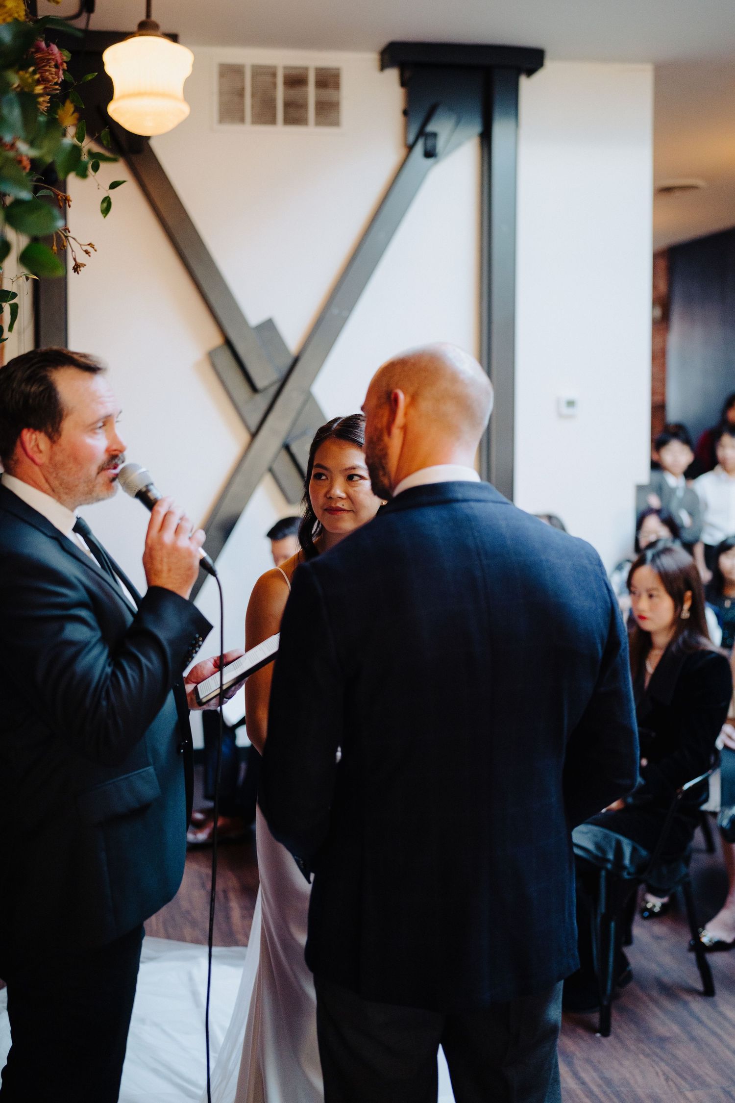 Wedding ceremony in progress with officiant and couple exchanging vows in front of gathered guests.