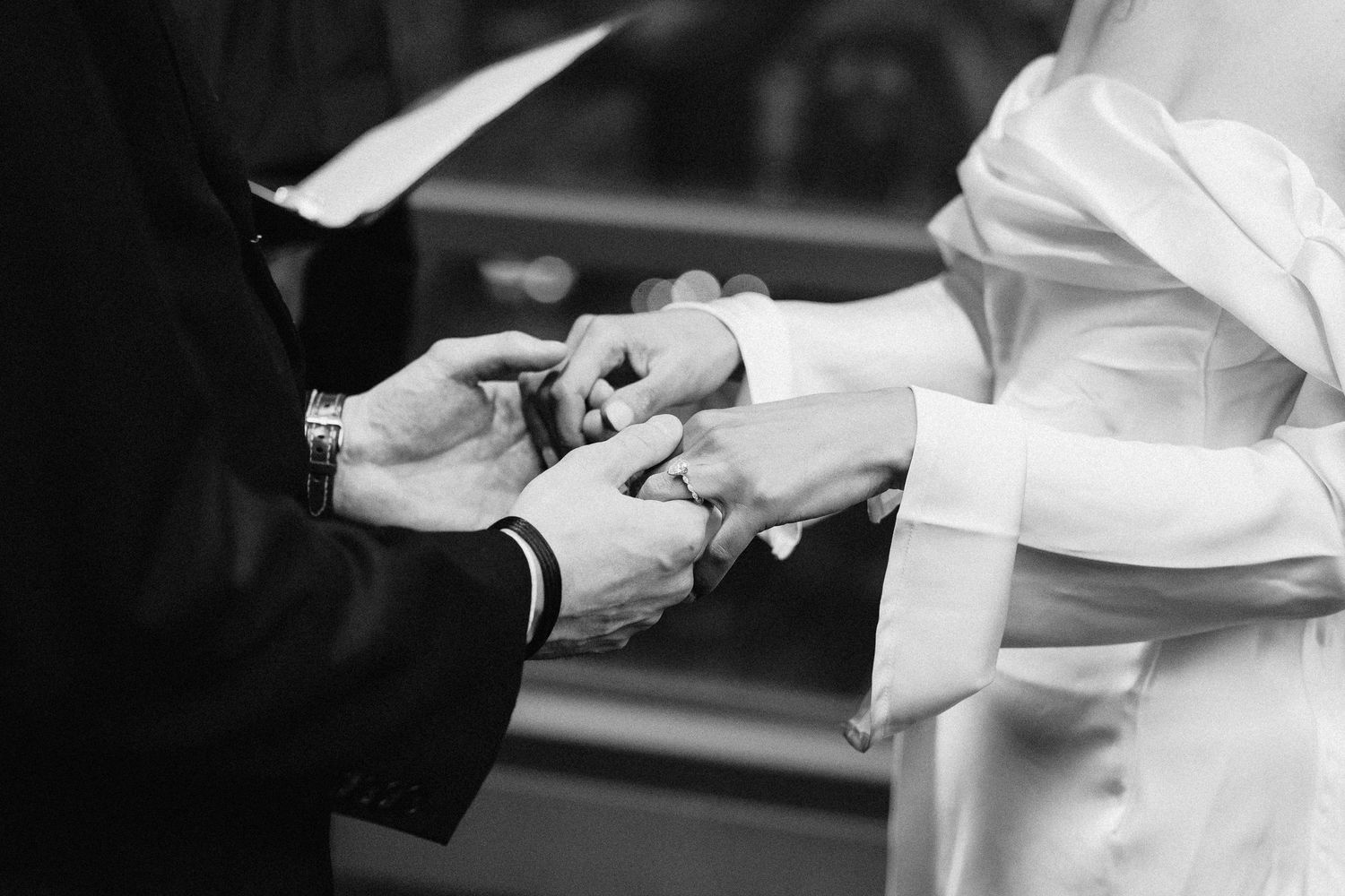 Close-up of wedding ring exchange ceremony showing hands and white dress details.